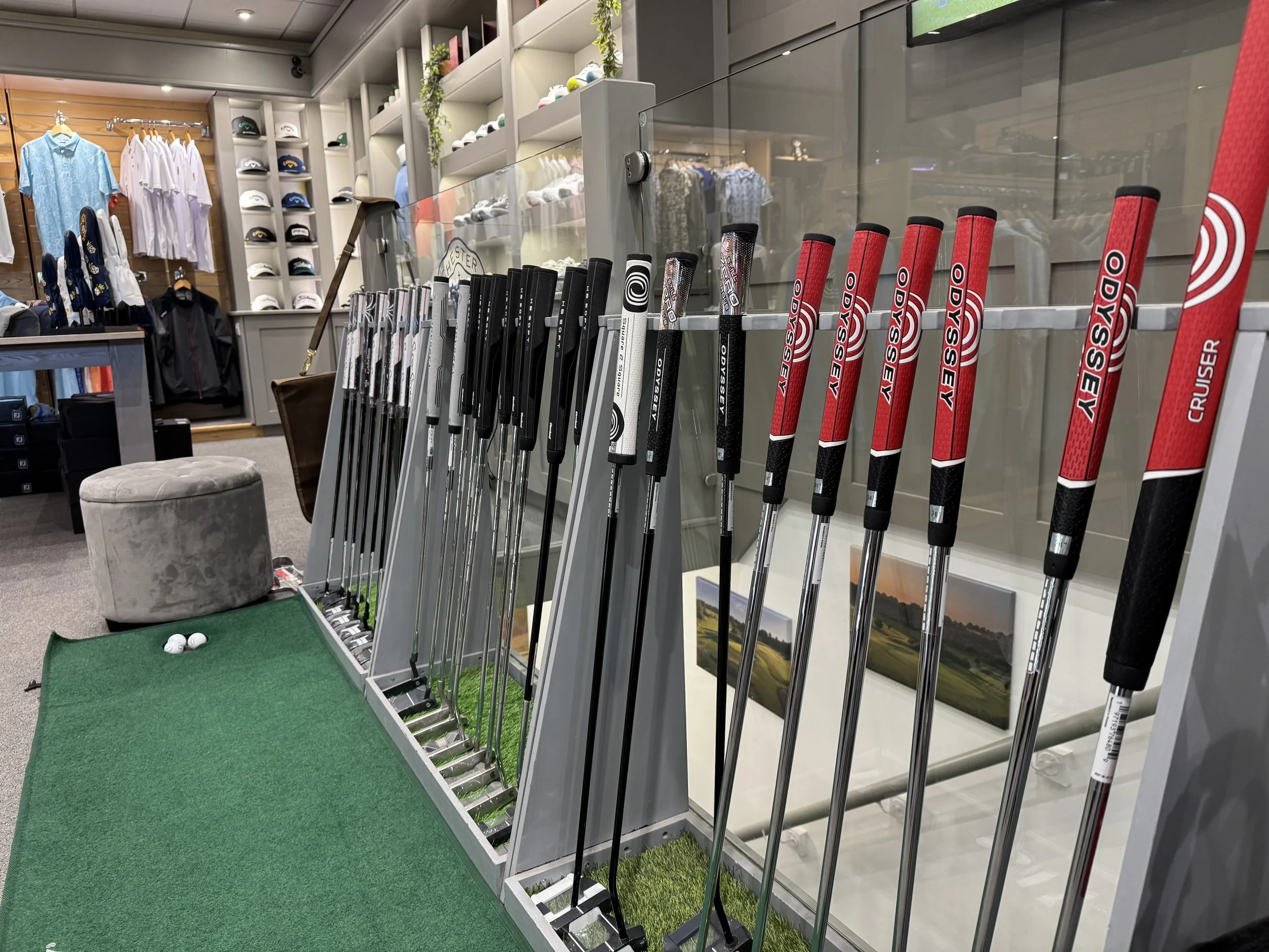 Golf clubs displayed in a store with clothing and accessories in the background.