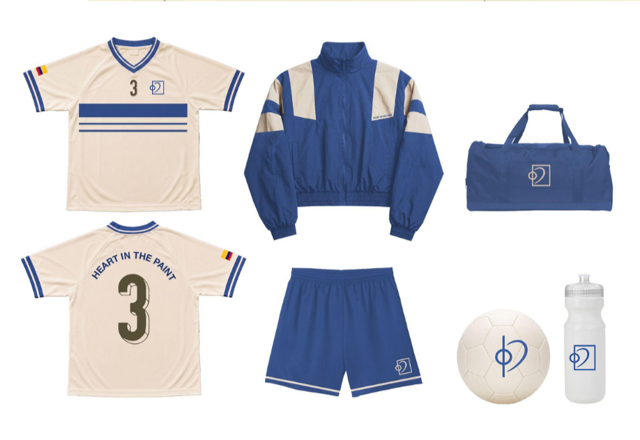 Conjunto de artículos de fútbol que incluye una camiseta de fútbol de color crema y azul con el número 3 y la inscripción «Heart in the Paint» en la espalda, una chaqueta de chándal azul y crema, unos pantalones cortos azules, un balón de fútbol blanco, una botella de agua blanca y una bolsa de deporte azul; todos ellos con un logotipo que muestra un círculo y una línea vertical.