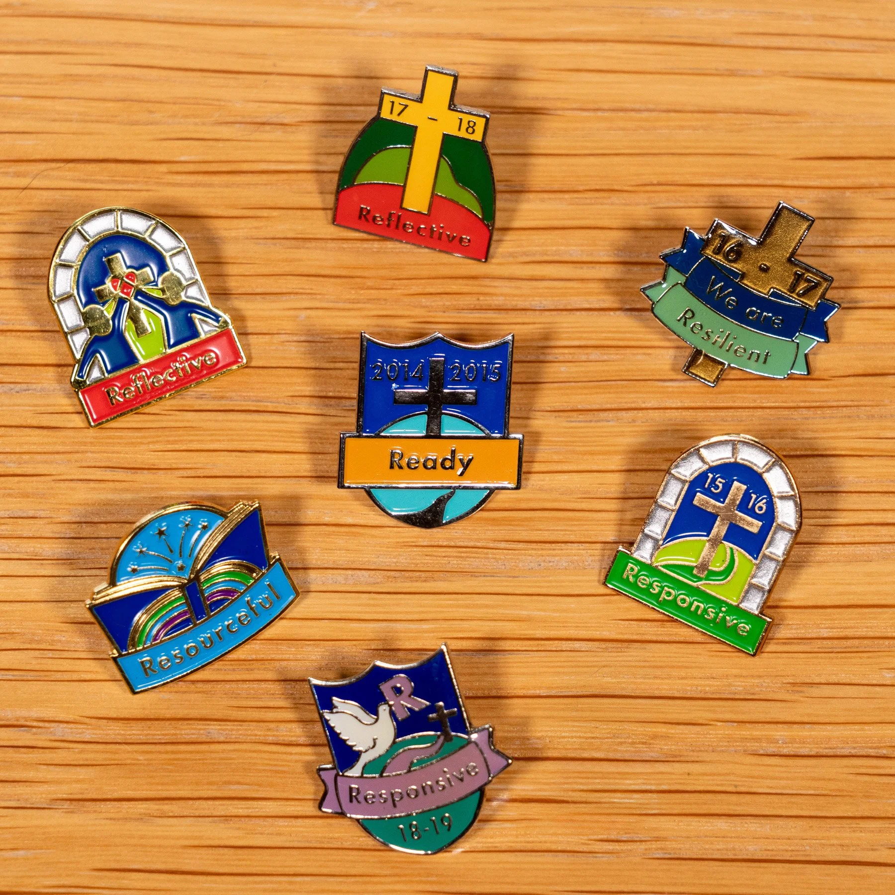 Collection of colorful pins with various symbols and phrases related to religious reflections, resources, readiness, and responsibility placed on a wooden surface.