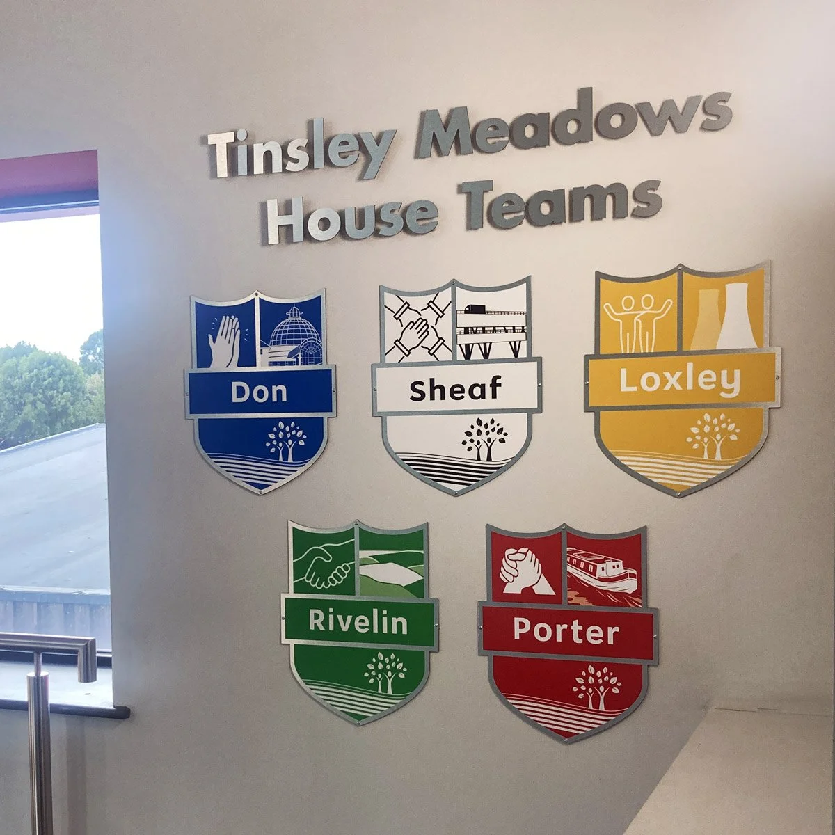 Wall display with 6 colorful badges representing different house teams at Tinsley Meadows school, including Don, Sheaf, Loxley, Rivelin, and Porter.