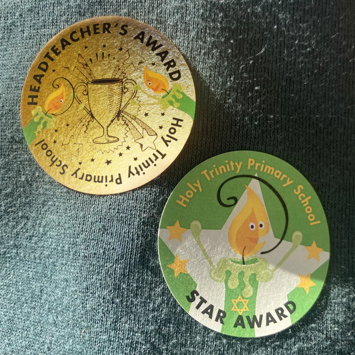 Gold Headteacher Award sticker and Star Award Sticker featuring school candle characters for Holy Trinity Primary School