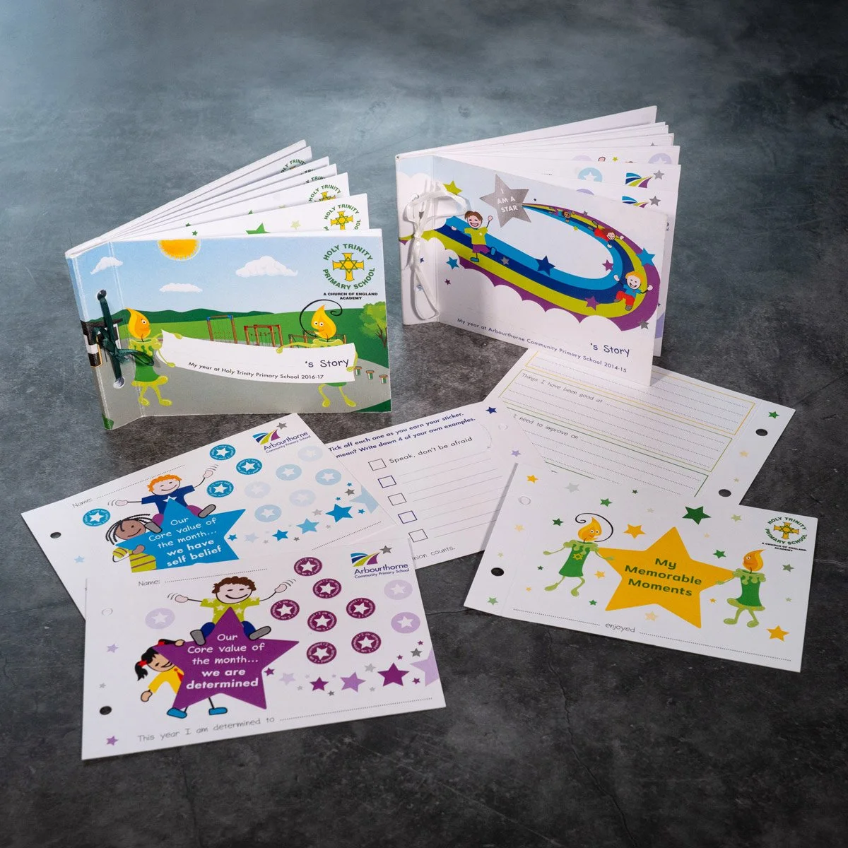 Open children's activity books and sheets from Holy Trinity Primary School, featuring colorful illustrations, kids’ stories, and self-belief charts, placed on a dark surface.