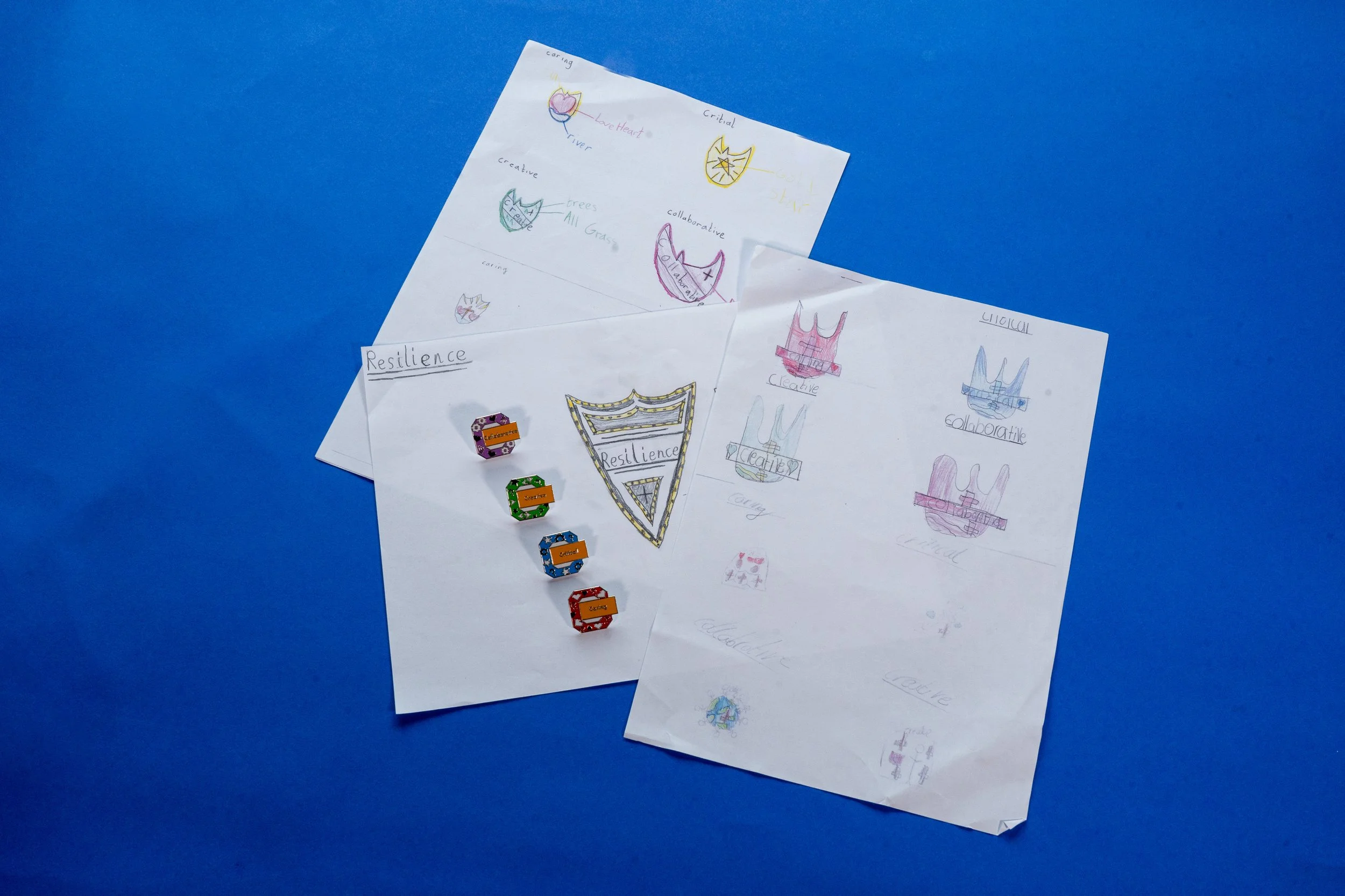 Two pages of hand-drawn sketches and notes on white paper placed on a blue surface, with small colorful blocks nearby.