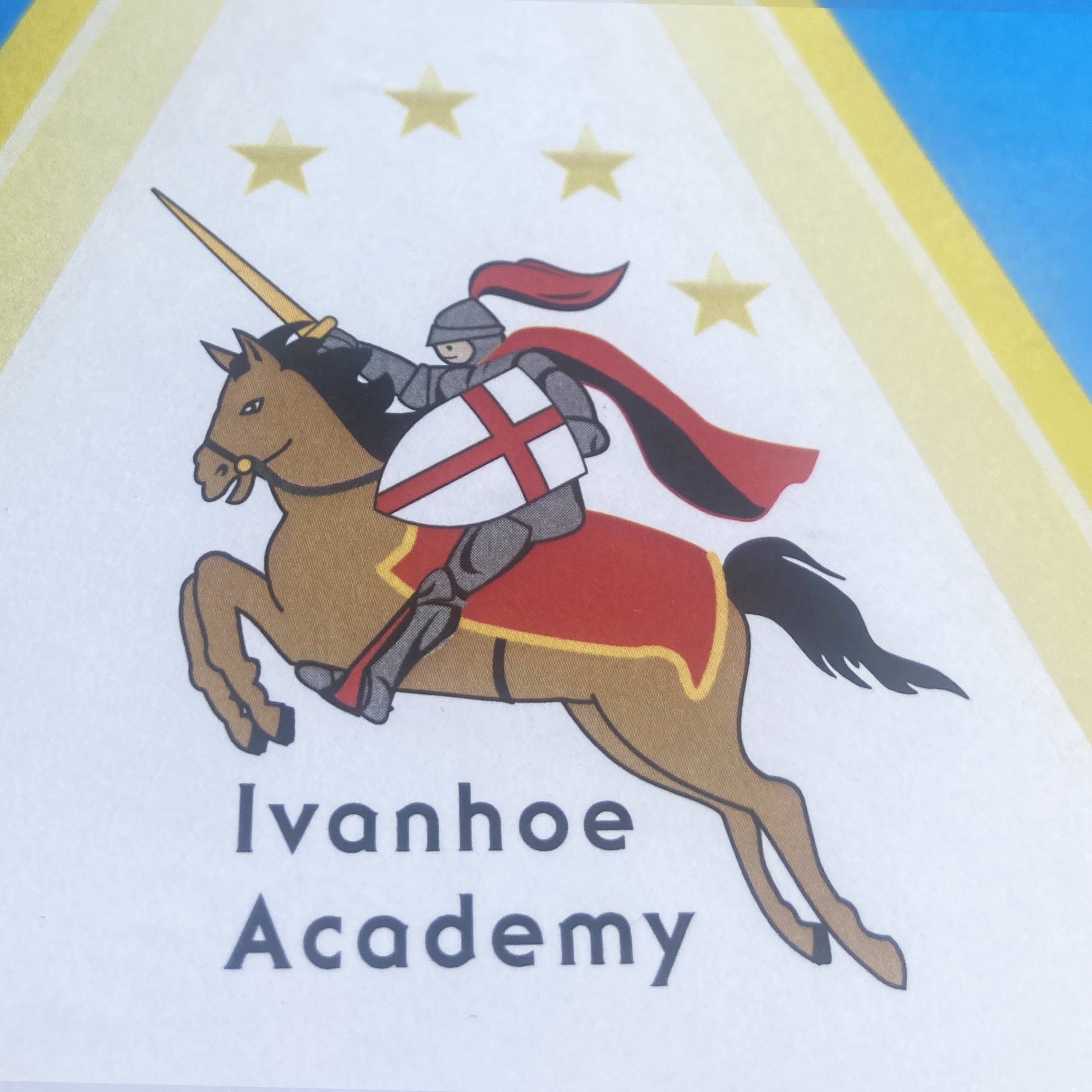 Close-up of a printed illustration of a knight in armor riding a horse, holding a lance, with yellow and blue decorative borders in the background and blurred text underneath.