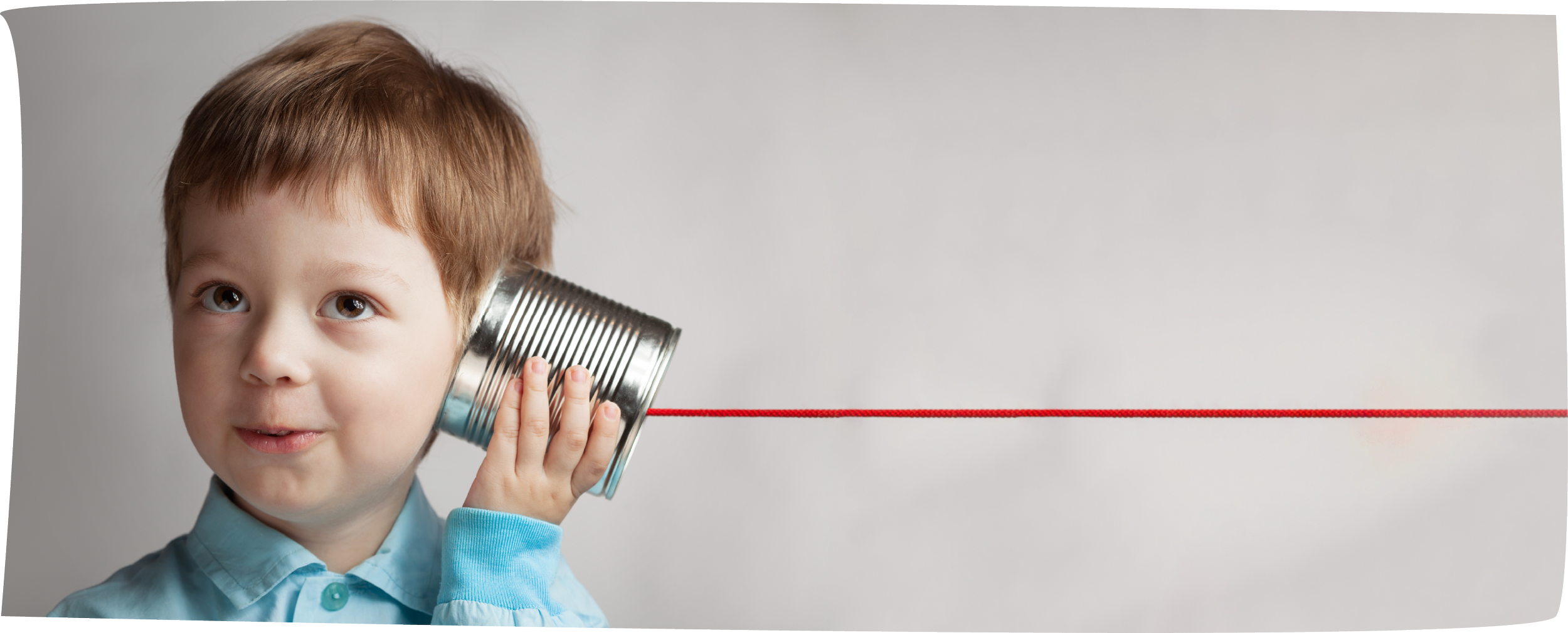 A young boy with brown hair holding a tin can phone to his ear, with a red string connecting to another point outside the frame, against a plain gray background.