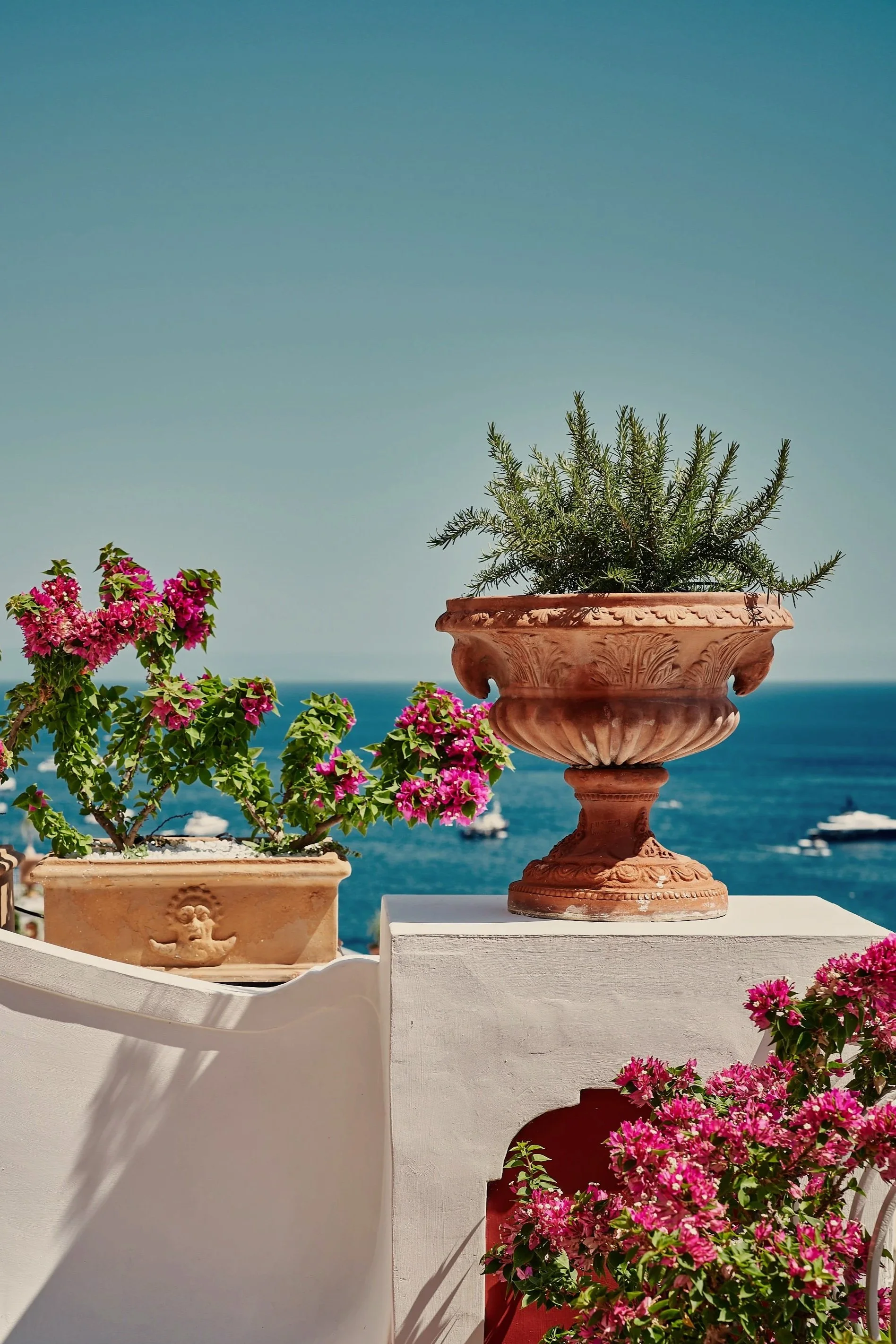 Le Sirenuse in Positano, Italy. Terrace with pink bougainvillea flowers in decorative pots, overlooking the sea and a boat in the distance.