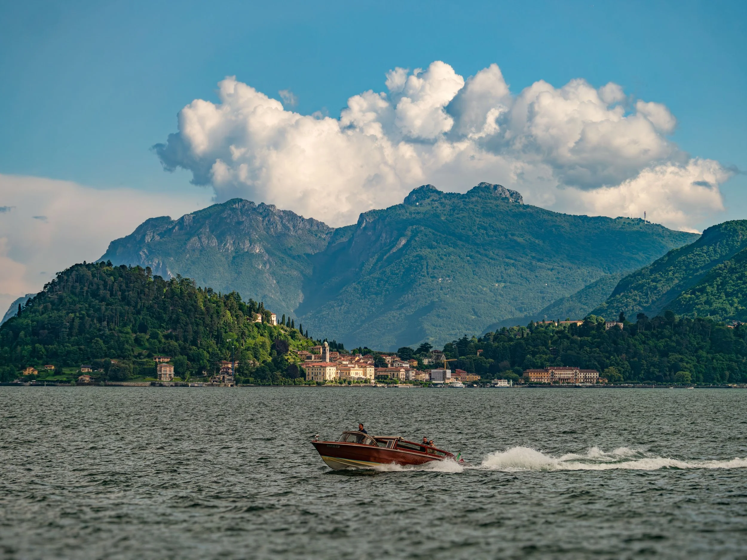 Menaggio, Lombardei, Italy on Lake Como. Motorboat cruising on Lake Como with mountain backdrop and Menaggio in view.