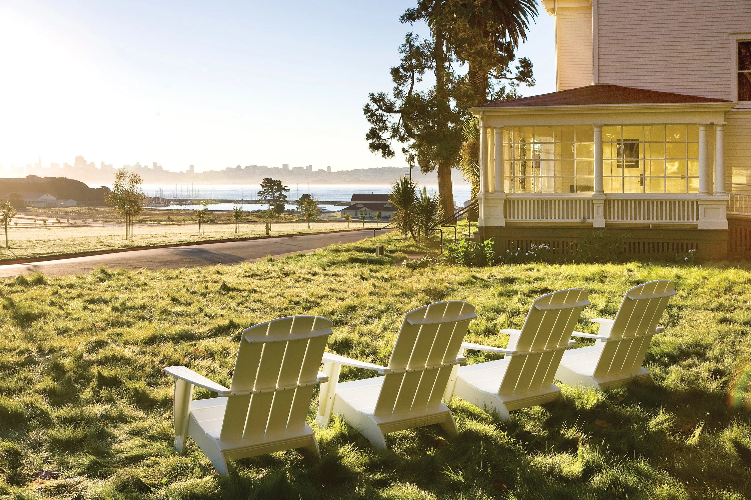 White Adirondack chairs on the lawn at Cavallo Point in Sausalito, with the historic yellow lodge and San Francisco skyline in the distance.