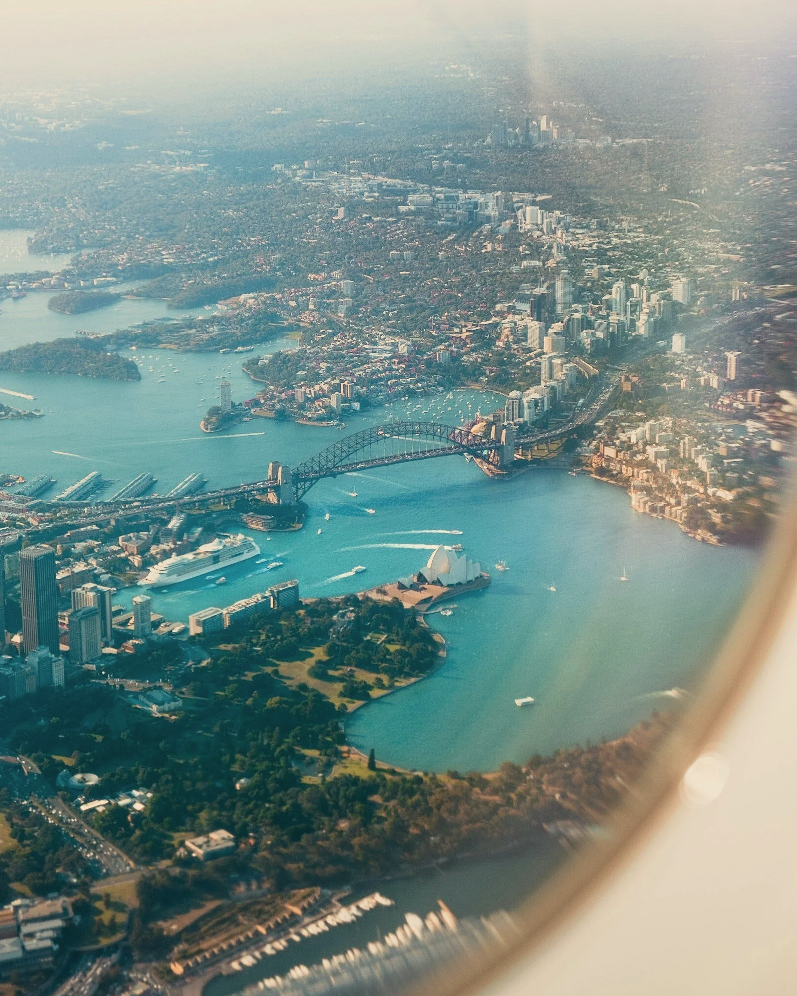 Aerial view of Sydney with the Sydney Harbour Bridge and Sydney Opera House in the foreground, and the city skyline and harbor with boats in the background.