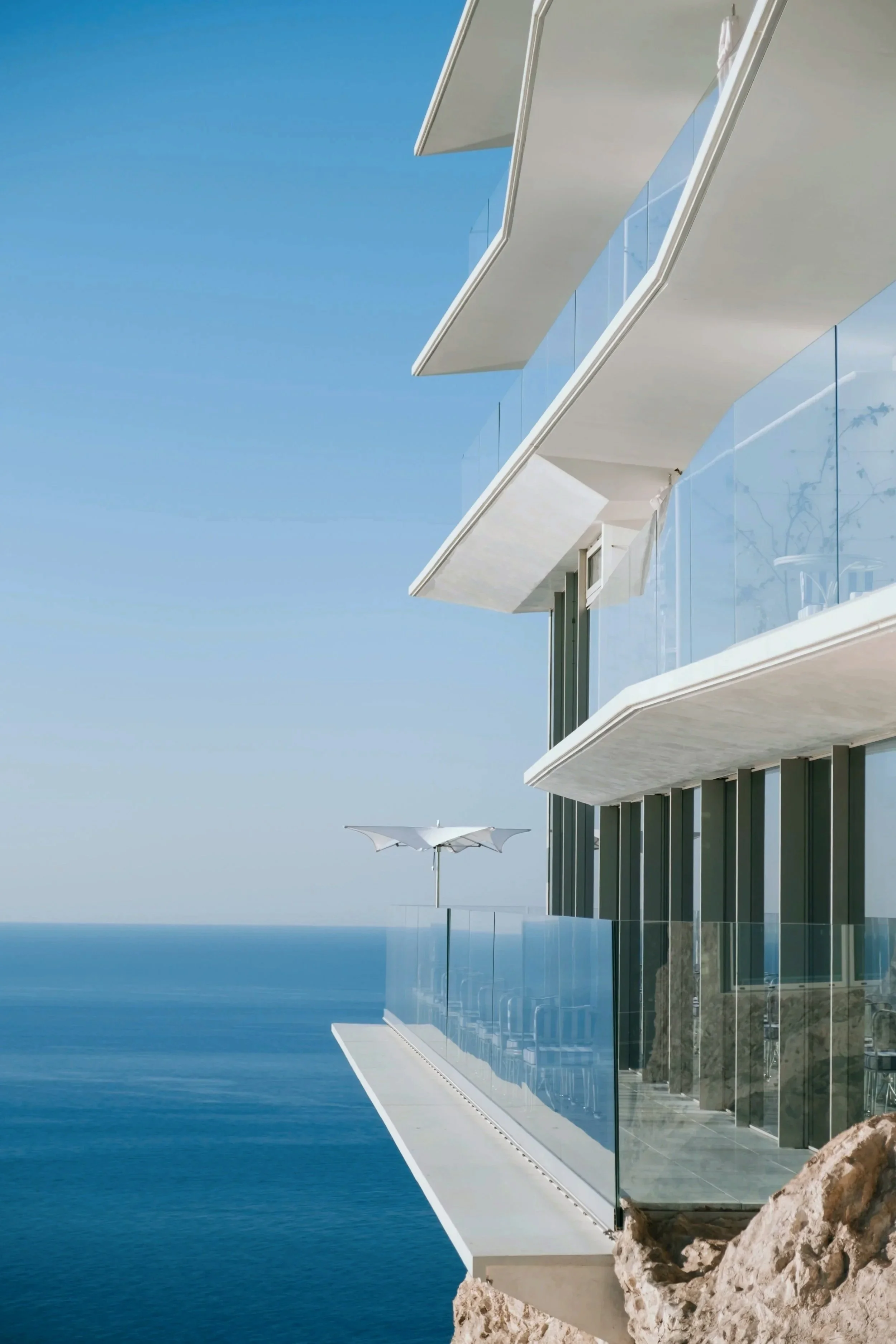 Modern glass-and-white balconies cantilevering over the cliffside at The Maybourne Riviera, framing panoramic Mediterranean Sea views on the French Riviera perched above Monaco.