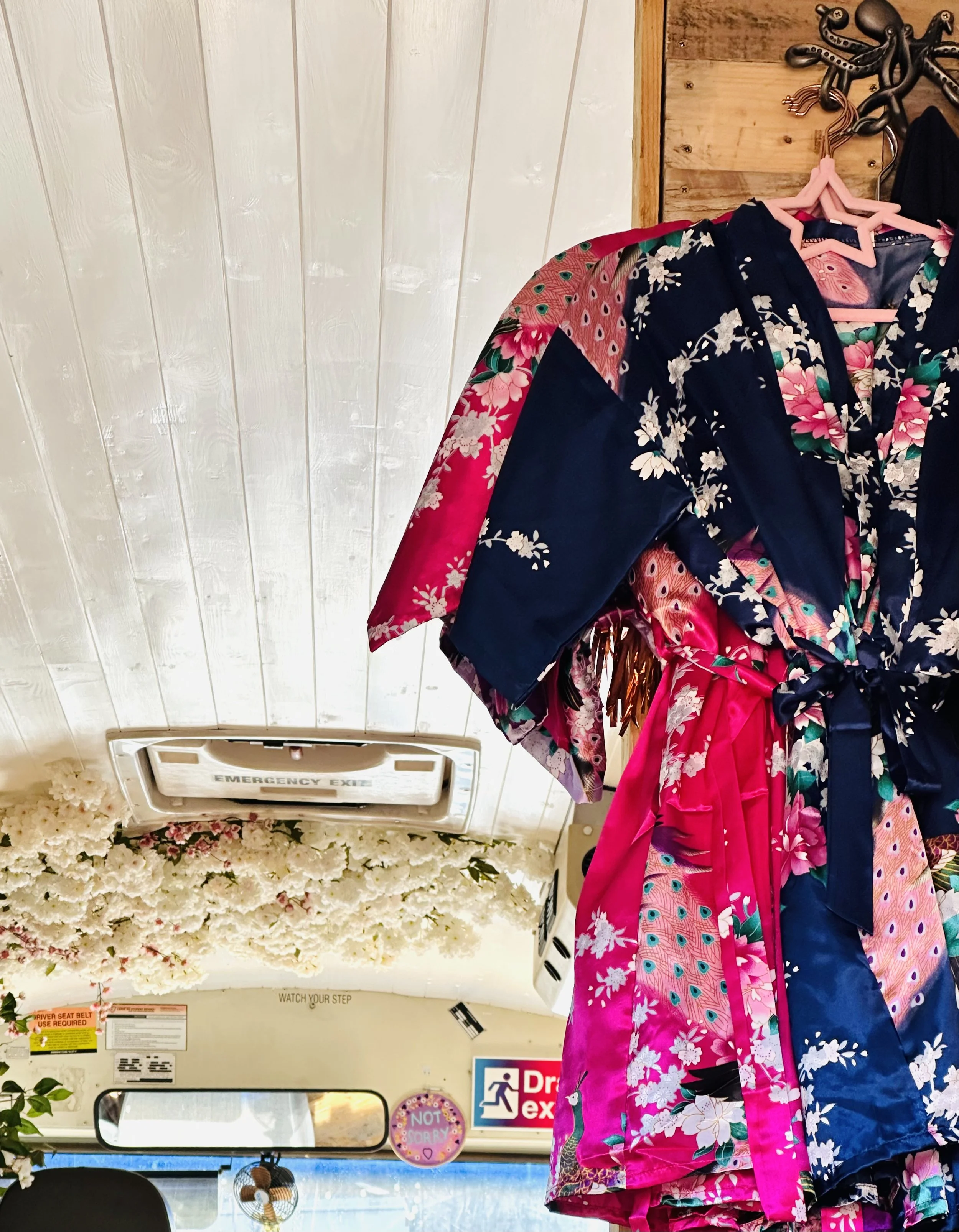 Hanging floral patterned robes or garments in pink, black, and green colors inside a shop or boutique, with wooden wall panels in the background
