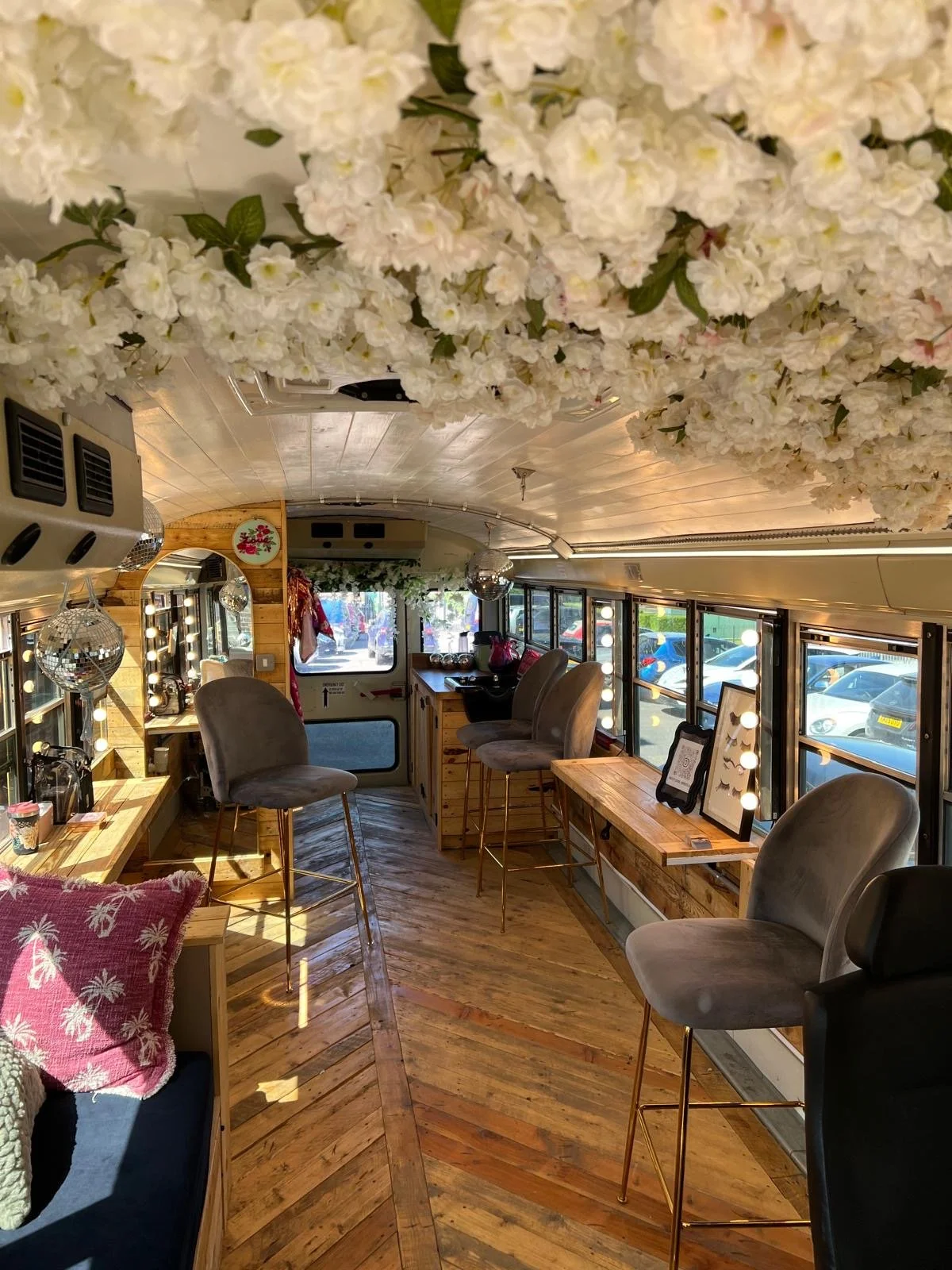Inside the decorated interior of a bus or van with wooden floors, chairs, and a ceiling decorated with white flowers.