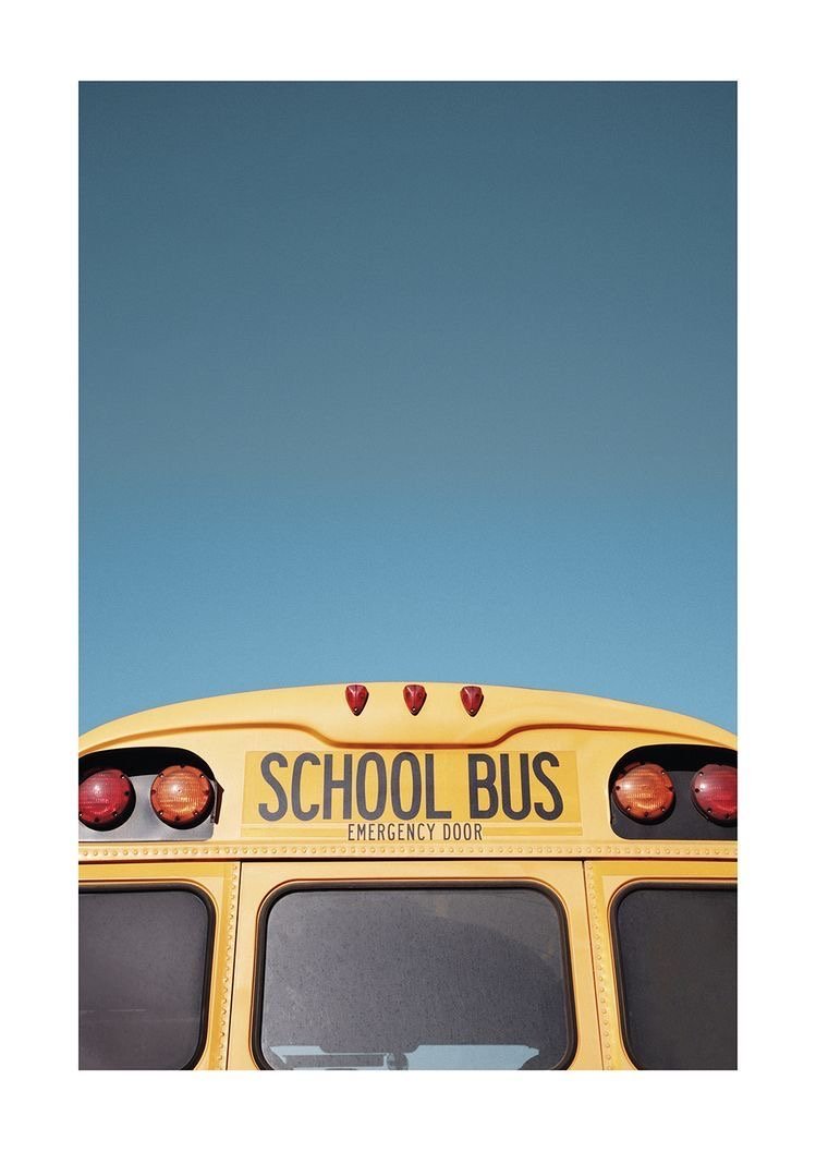 Close-up of the front of a yellow school bus showing emergency lights, an emergency door sign, and the top part of the windshield against a clear blue sky.