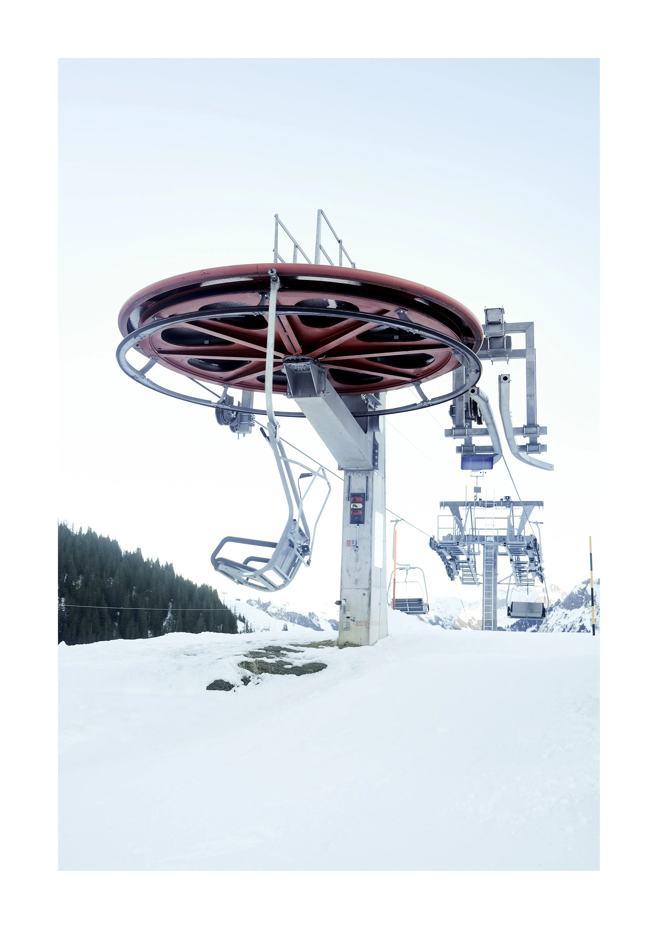 An empty ski chairlift on a snowy mountain with a forest and mountain range in the background.