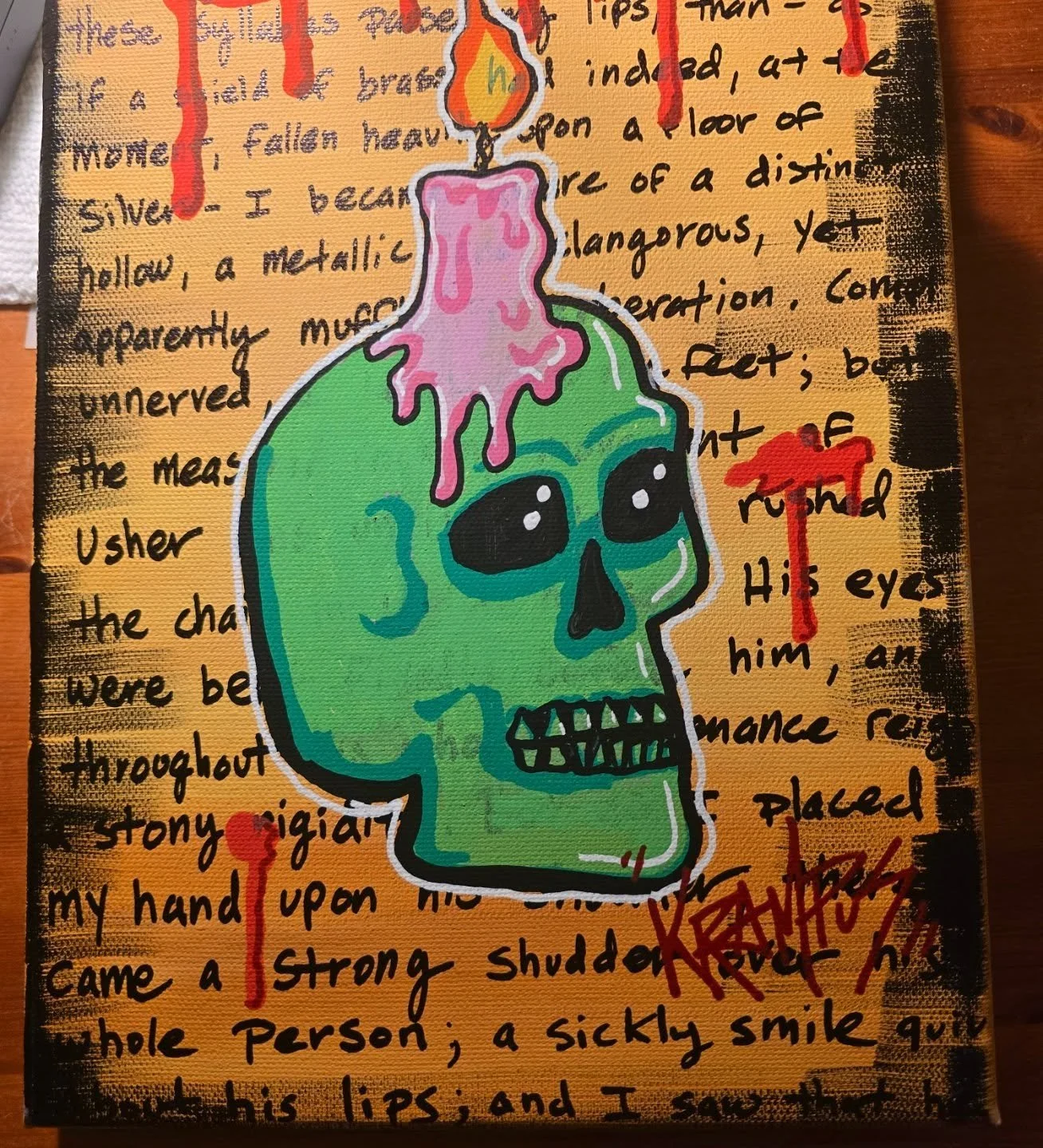 A colorful illustration of a green skull with black eye sockets and a pink melting candle on top. The background contains handwritten text on an orange canvas with black ink and red paint splatters.