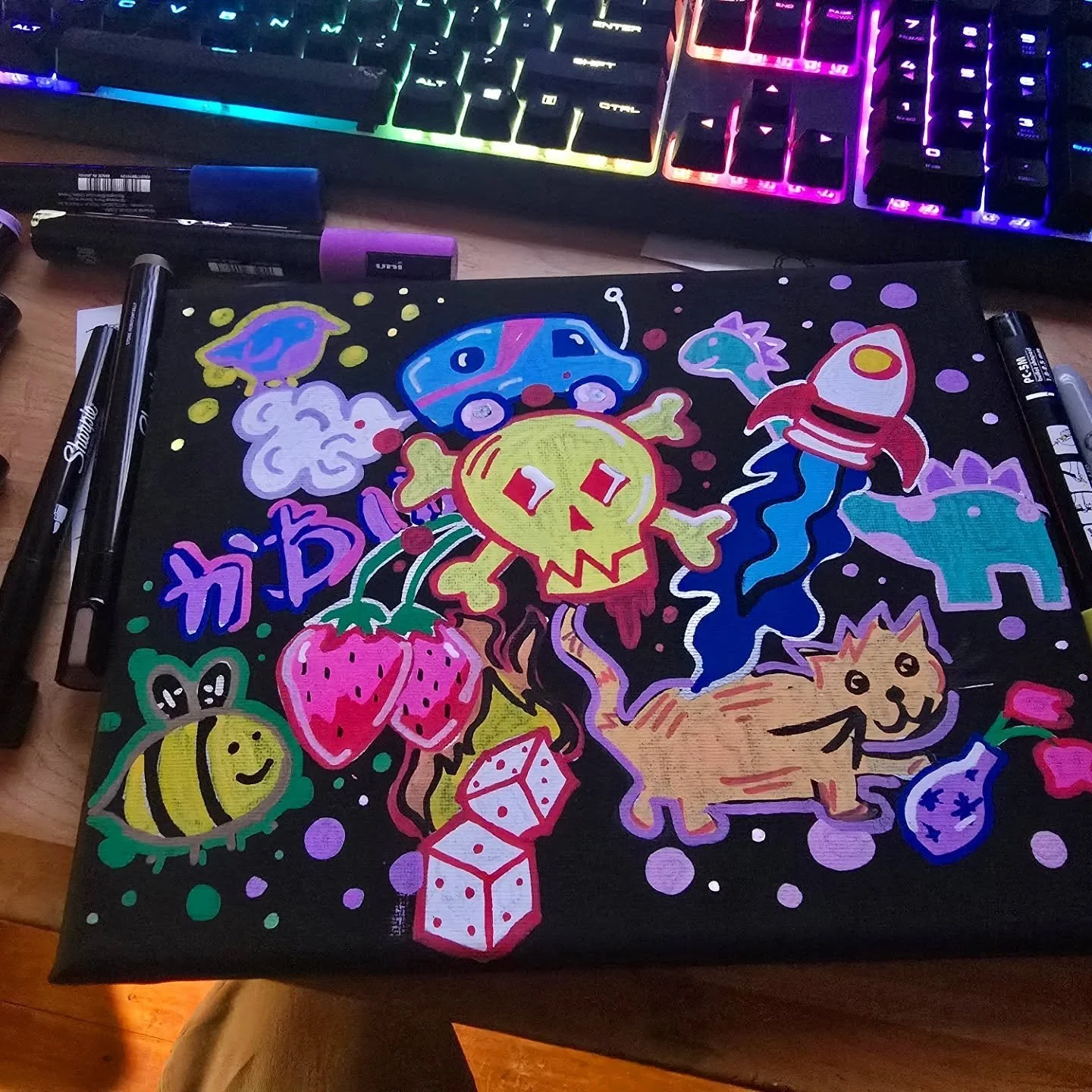 Colorful neon-style drawing featuring a pumpkin skull, a strawberry, a bee, a crate, an elephant, a dog, a rocket, a fish, and other whimsical elements on a black background, with markers on the sides.