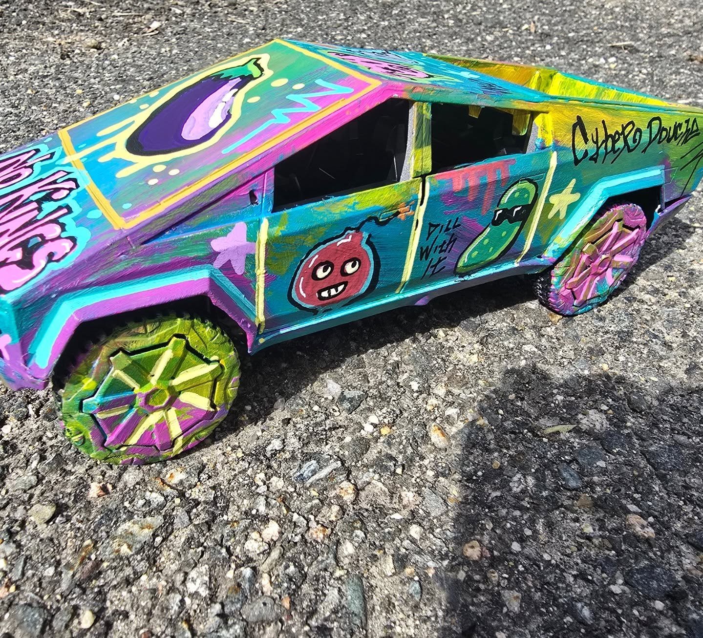 Colorful, hand-painted toy car with graffiti-style art, cartoon characters, and bright patterns on the wheels, placed on asphalt.