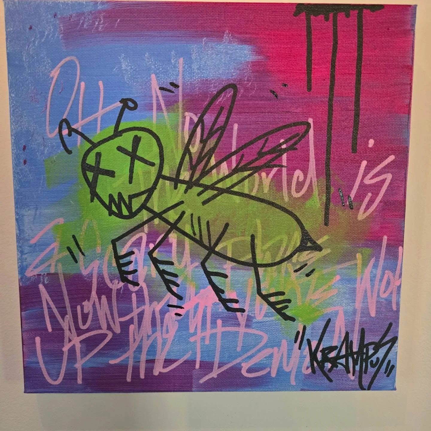 Graffiti art featuring a cartoonish green insect with large wings, head with antennae, and X's for eyes, drawn with black lines on a colorful spray-painted background of pink, purple, green, and blue with scribbled pink and white tags.