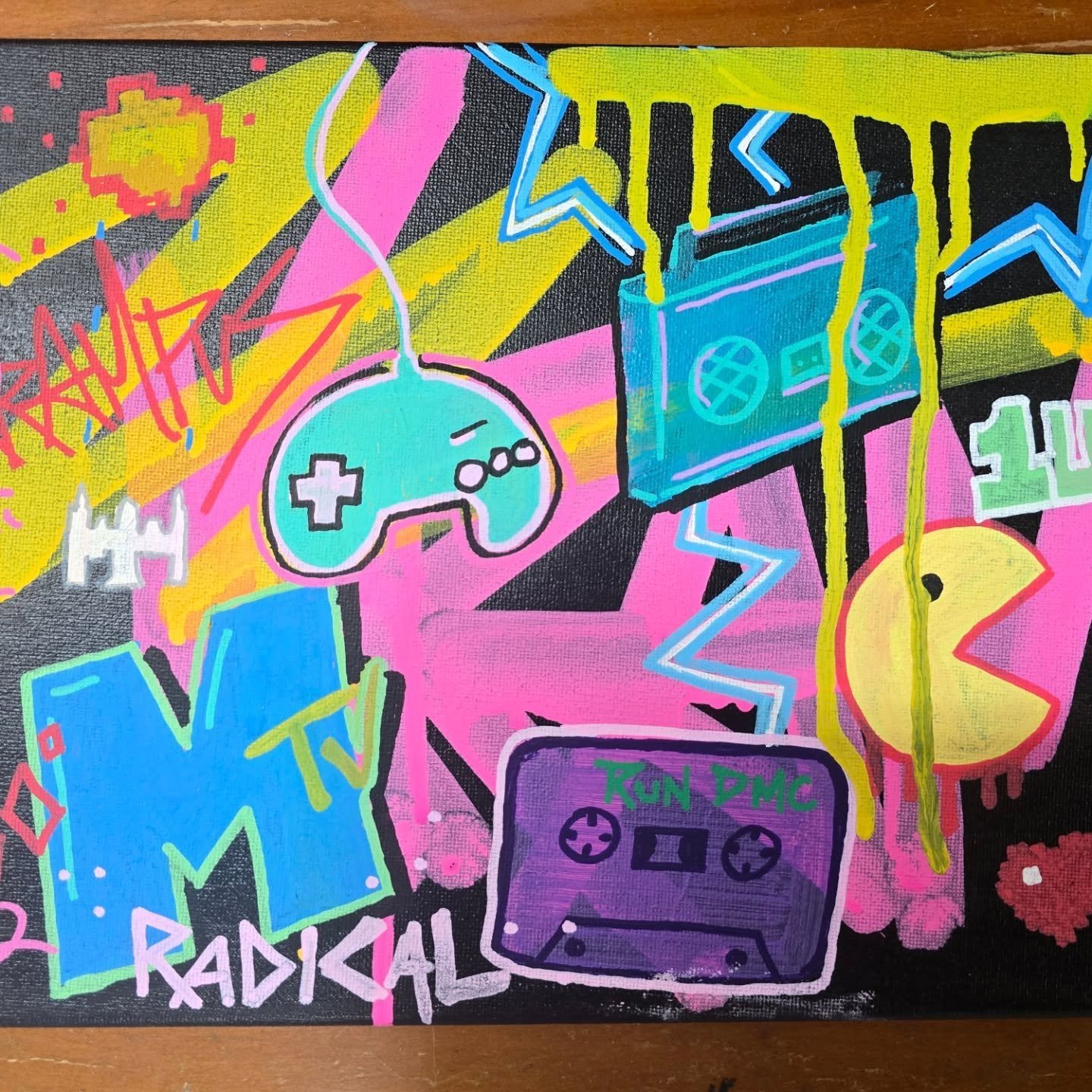 Bright, colorful graffiti-style artwork featuring a game controller, a cassette tape labeled "Kun DMC," a blue smartphone, a yellow Pac-Man character, a retro TV with "TV" written on it, a pixelated white castle, and various lightning bolts, stars, a
