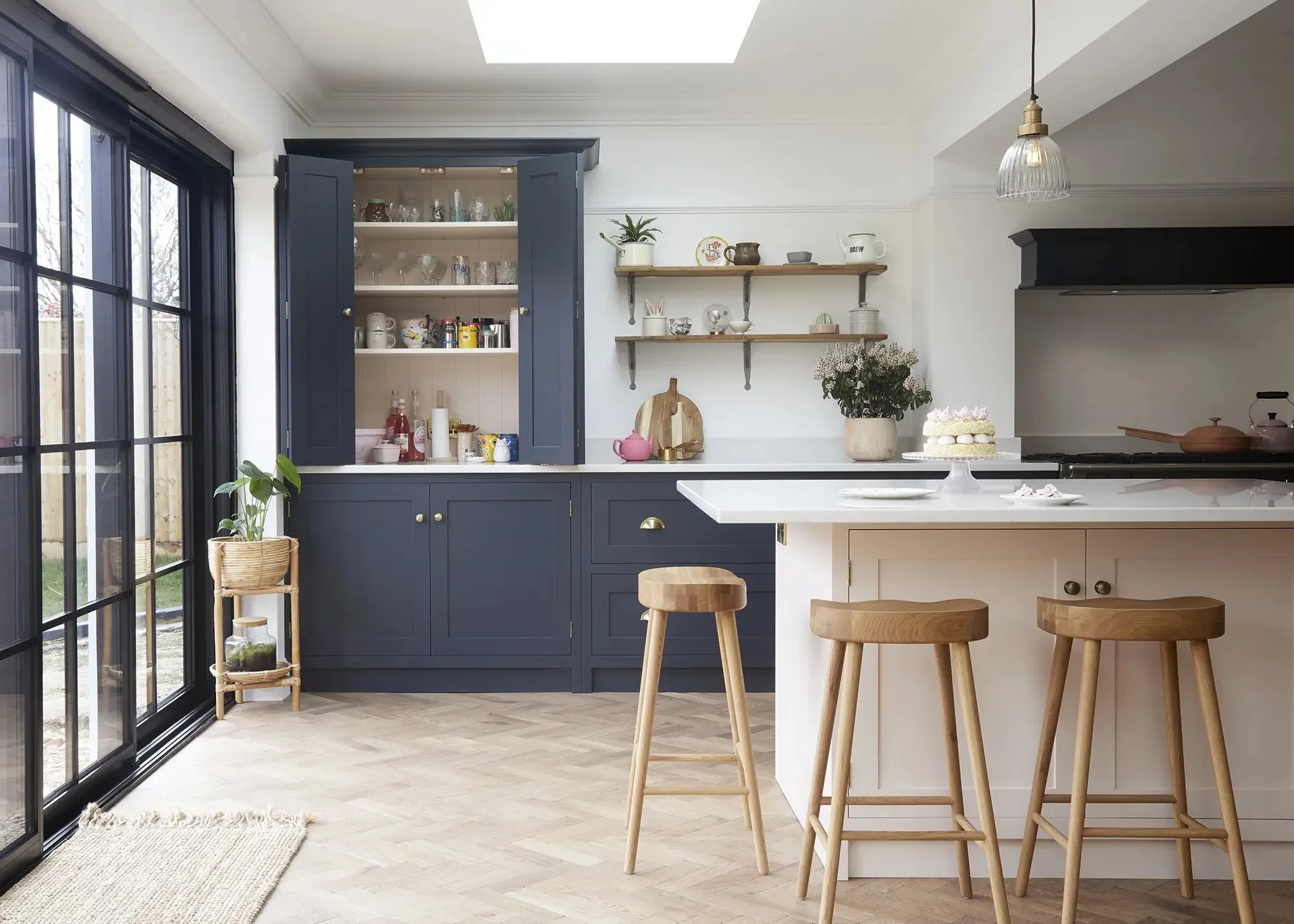Kitchen with navy cabinets, open shelving, wooden bar stools, large sliding glass door, and a white countertop with a cake on it