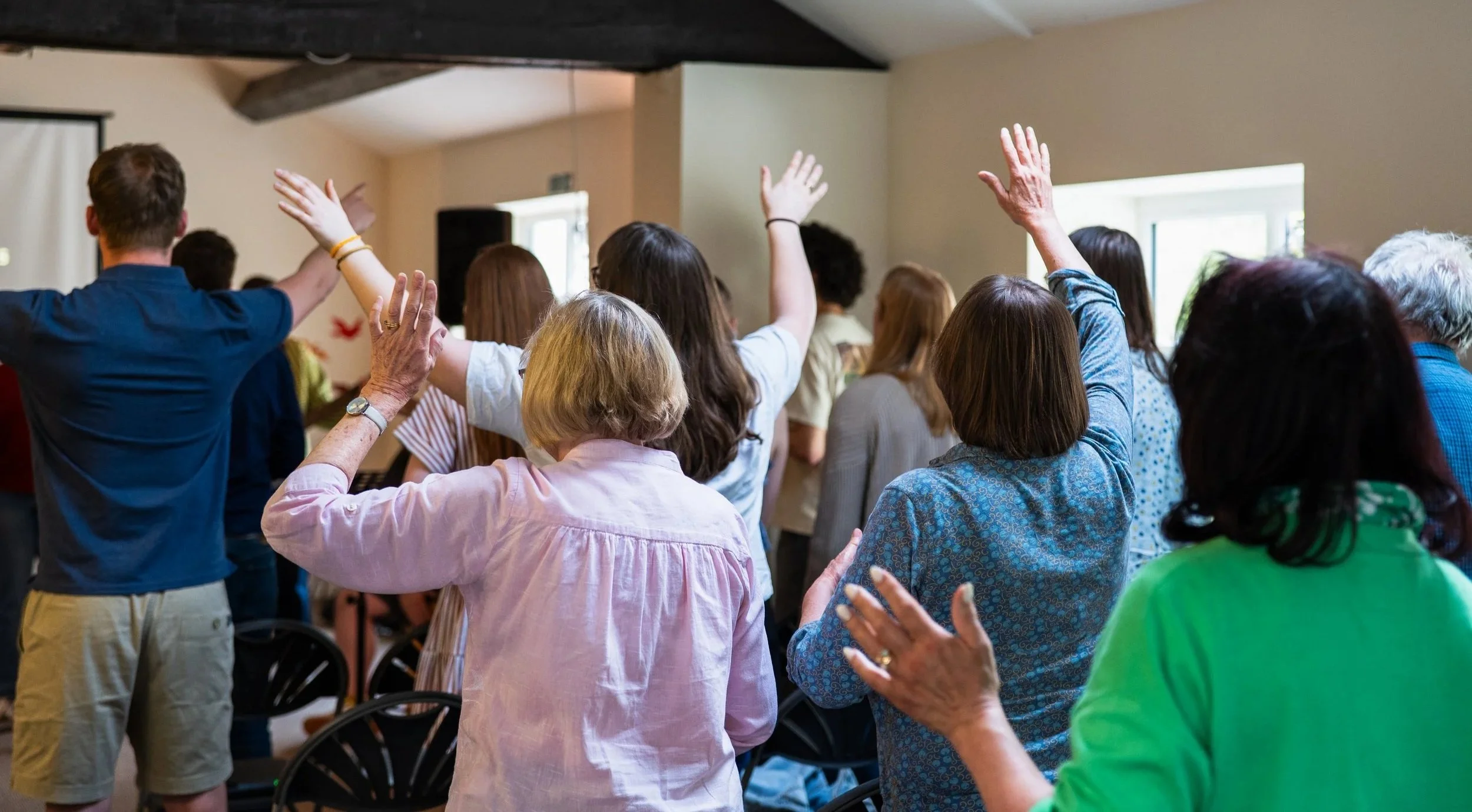 Group of mixed people attending a meeting with several individuals raising their hands during worship.