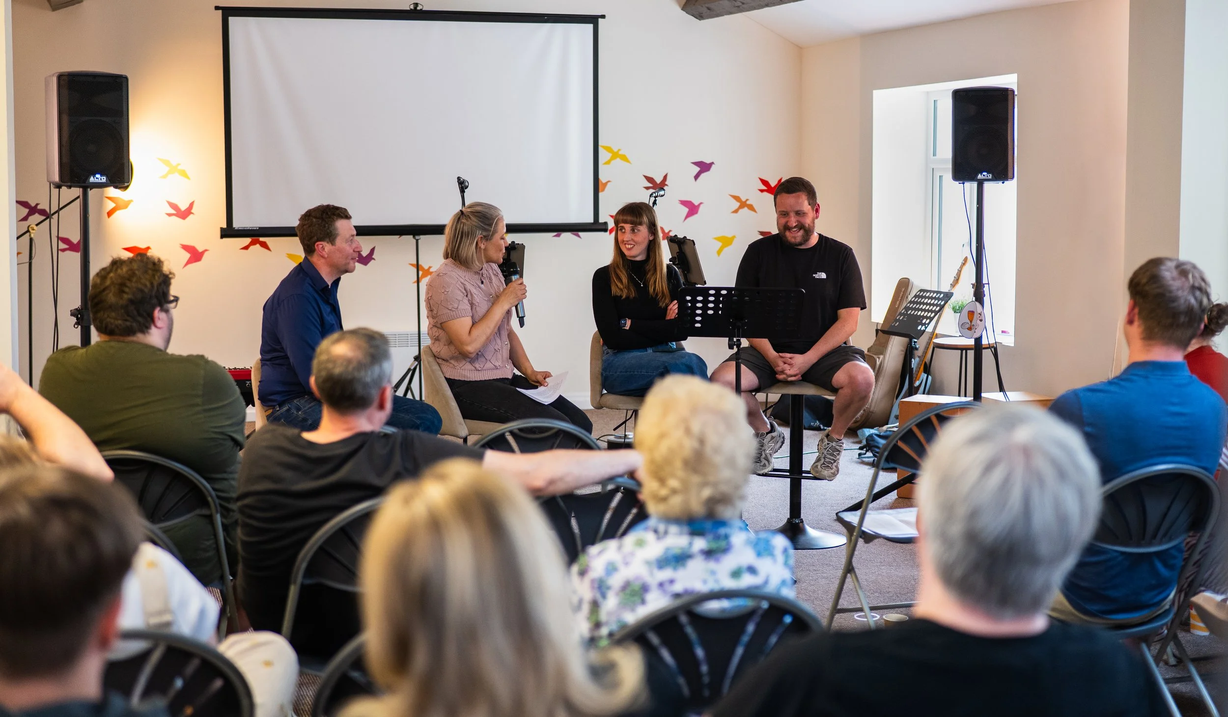 A group of leaders being interviews during a Sunday meeting. People in the congregation are smiling and laughing.
