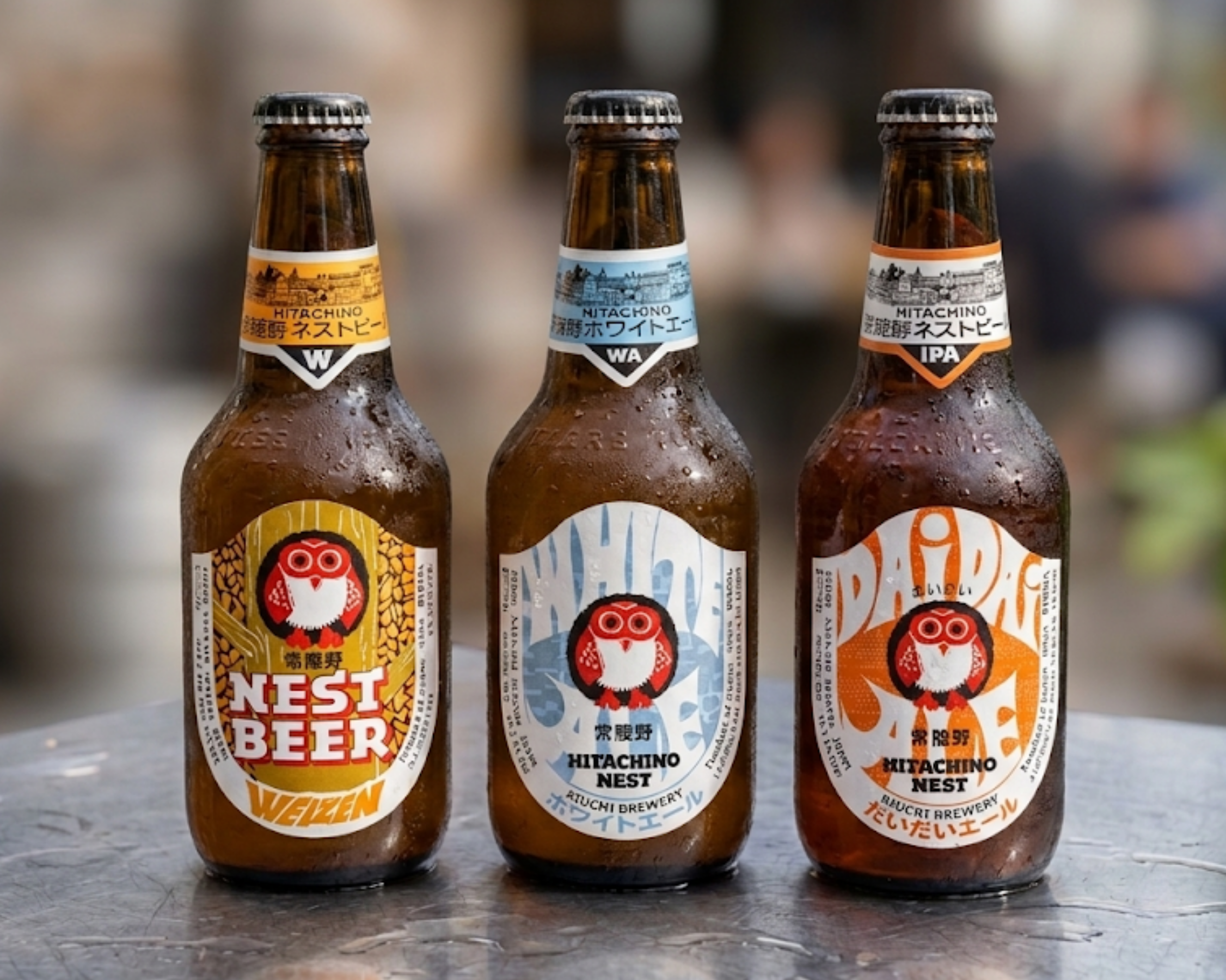 Three bottles of beer with Japanese labels, labeled Hitachino Nest Beer, placed on a dark surface.