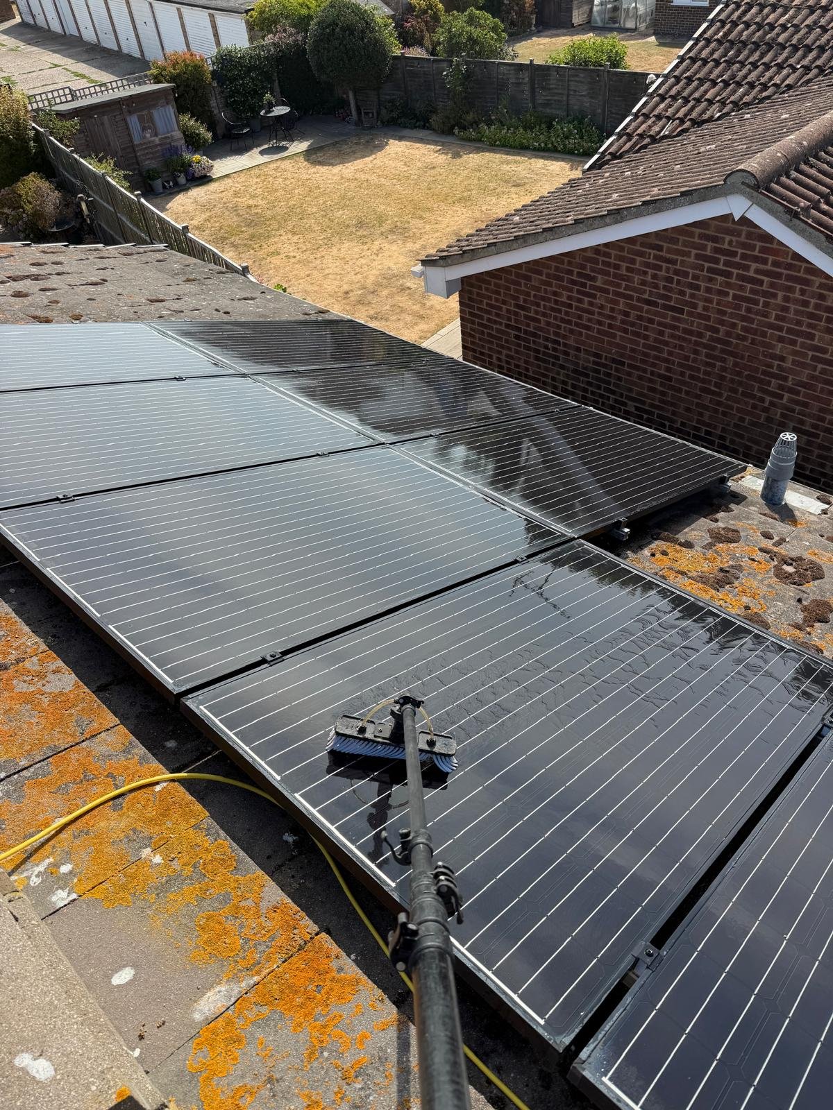Solar panels installed on a rooftop with a garden and backyard visible in the background.