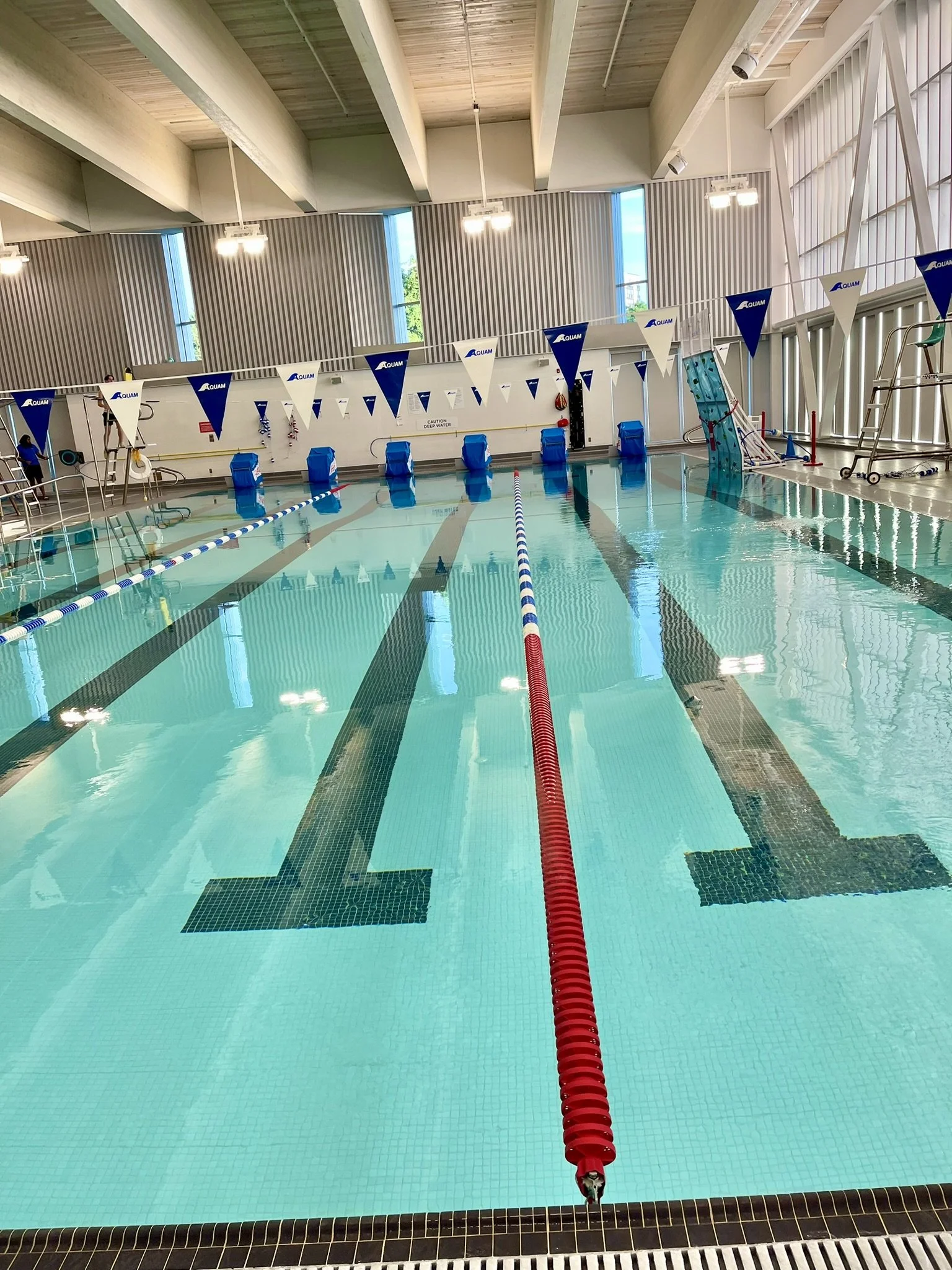 Indoor swimming pool with lane dividers, starting blocks, and a red rescue tube near the wall.