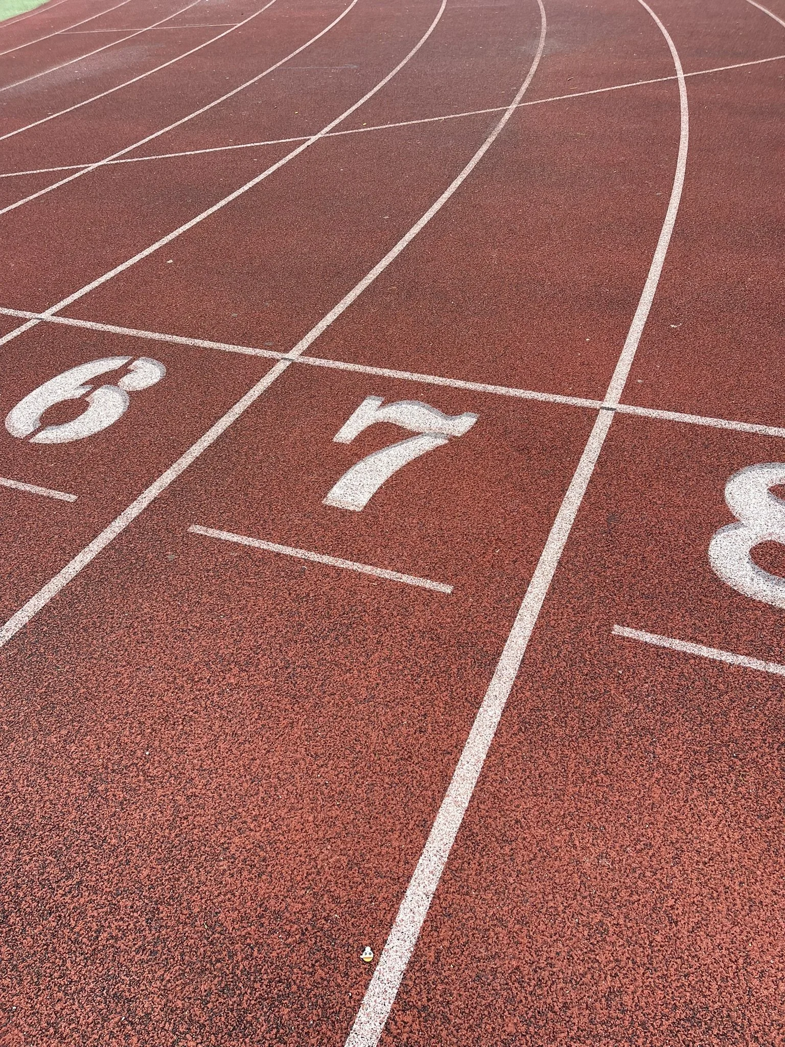 A red running track with white lane markings numbered 6 and 7, and a small cartoon-style figure at the bottom center.