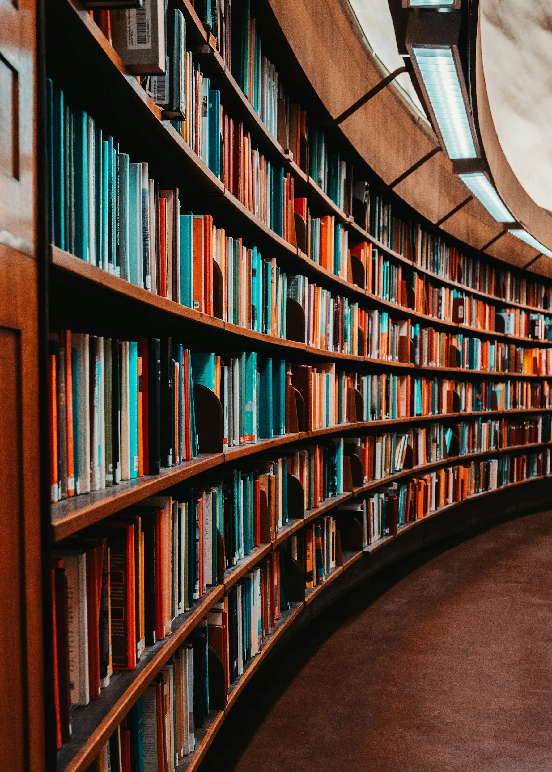 Curved wooden bookshelf filled with colorful books in a library.