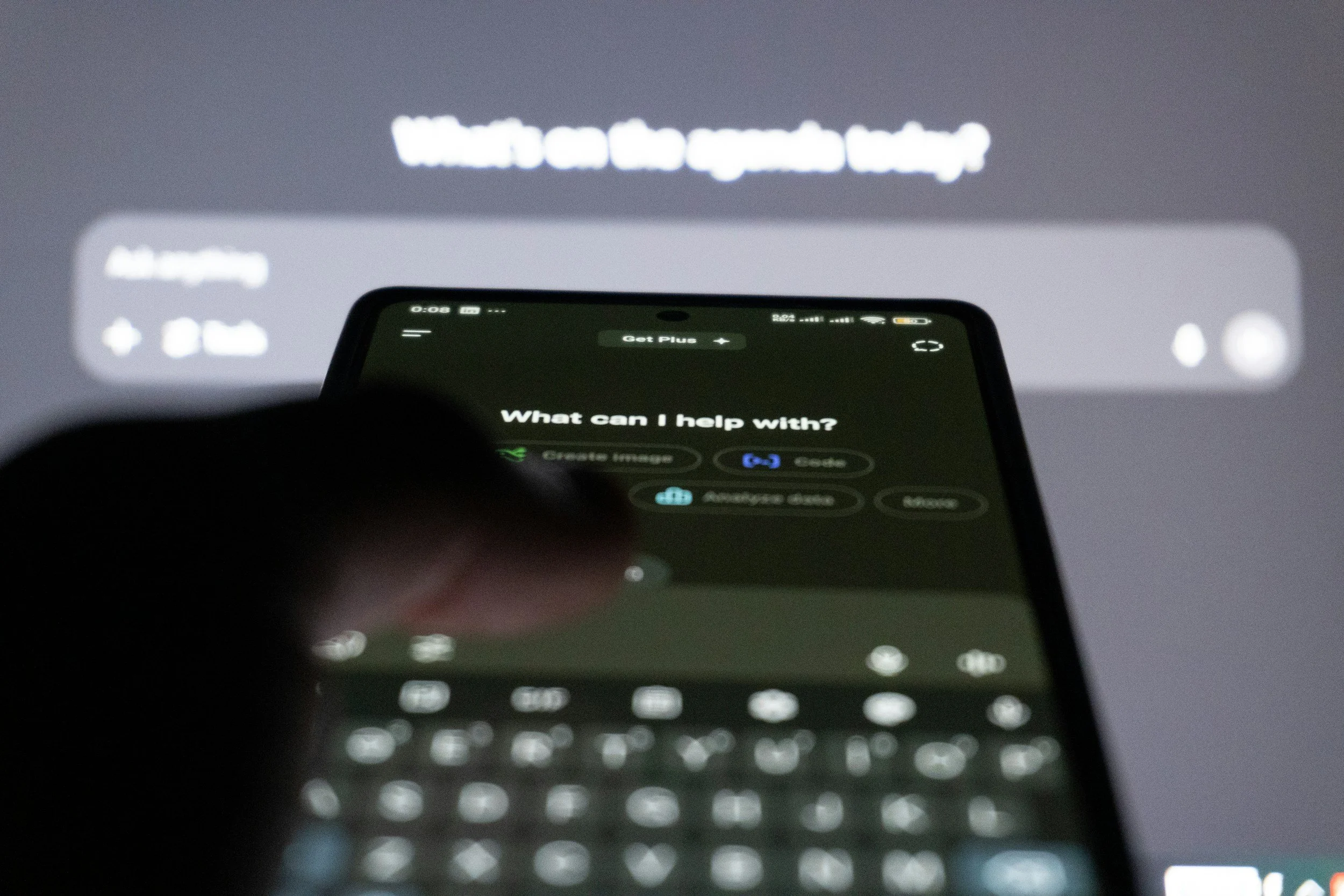 Close-up of a smartphone screen displaying a virtual assistant interface asking 'What can I help with?', with blurred text in the background.