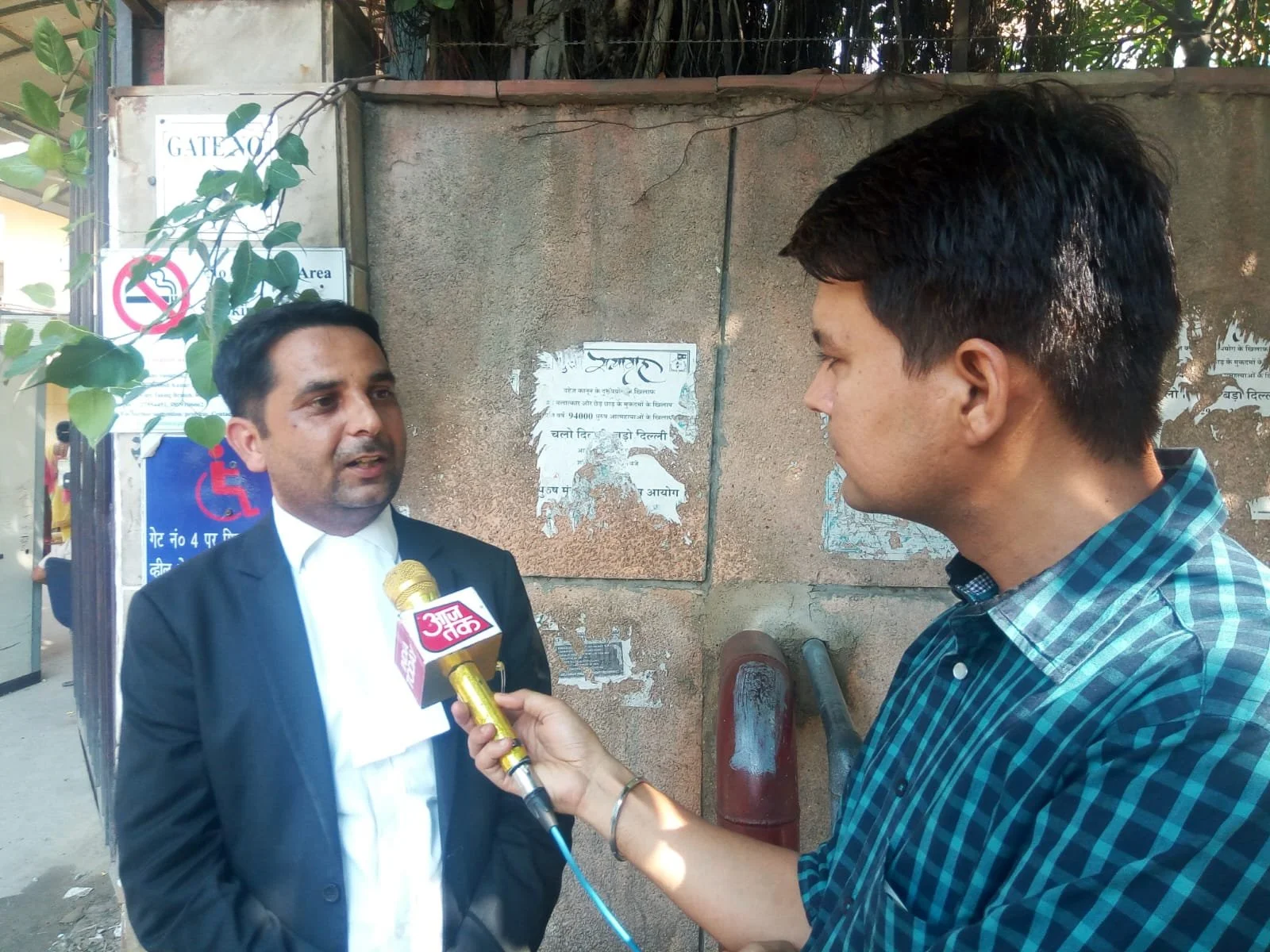 Advocate Manoj Rana , with a black coat and white collar, being interviewed by a reporter holding a microphone with the logo of Ajj Tak News