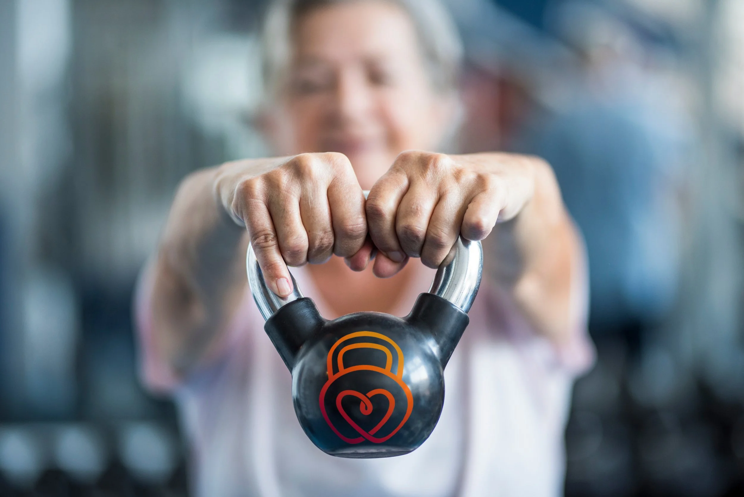 A person holding a kettlebell with a heart-shaped logo on it at the gym.  Personal Training for the over 50's. Ramsbury, Wiltshire.