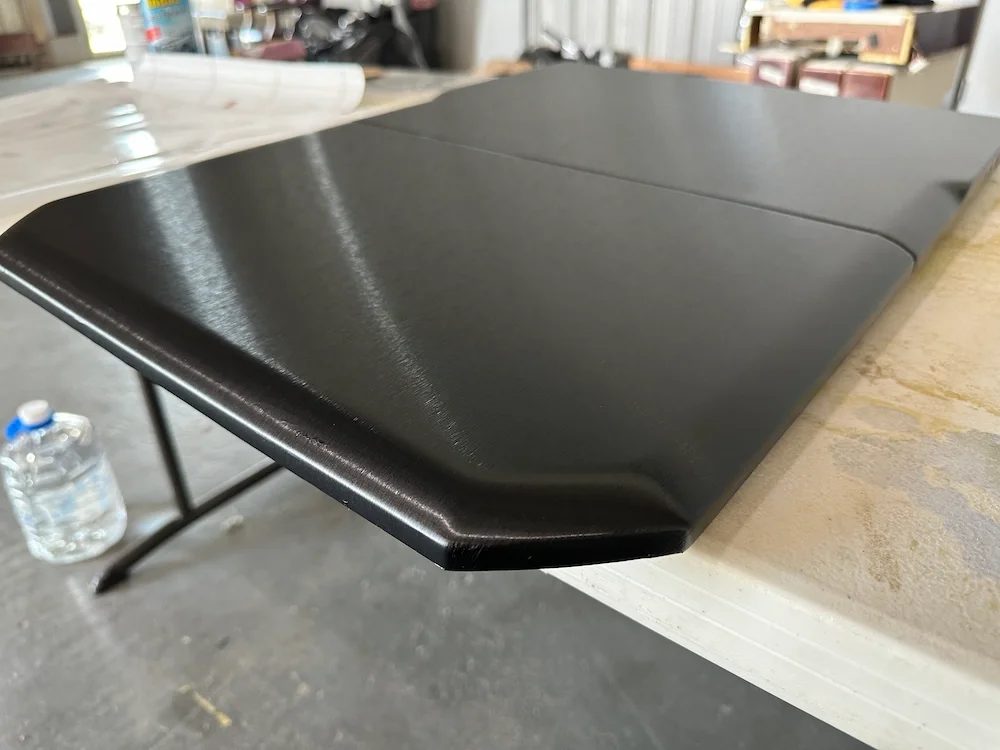 Close-up of a black laptop with a matte finish resting on a white table in a workshop or garage setting.