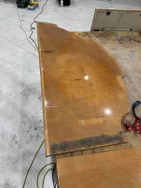 A wooden table with a damaged edge showing water damage and discoloration, situated on a concrete floor in a workshop or garage.