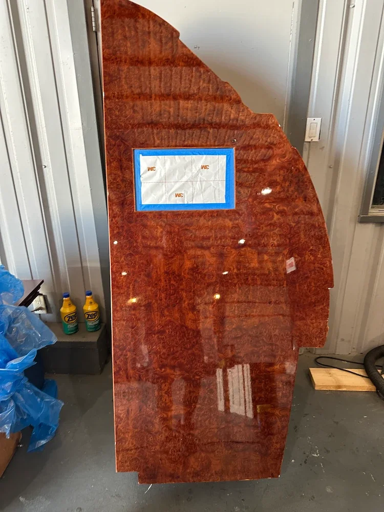 A polished wooden door with a curved top, with a small rectangular window covered with tape, standing in a workshop.