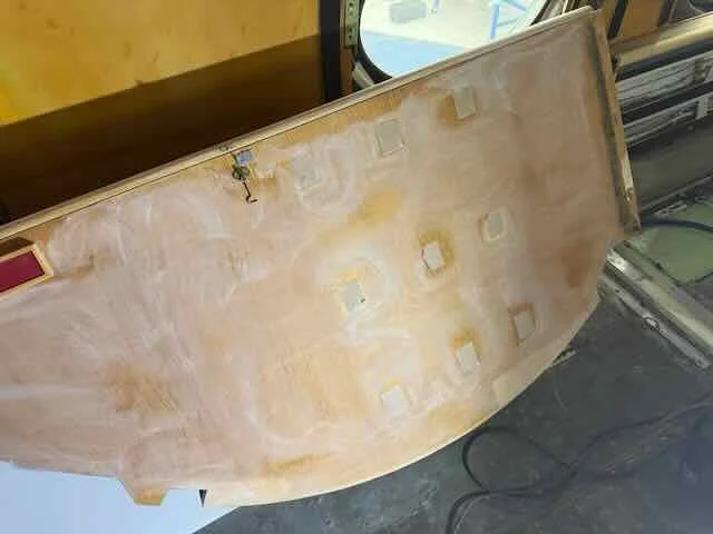 A large piece of wood or particleboard with multiple cut-out holes, leaning against a wall or another surface, with some yellowish stain marks on it.