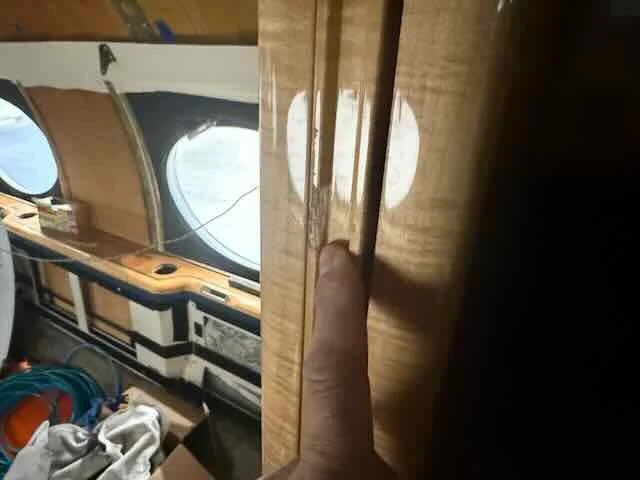 Close-up of a person inserting their finger into a small gap in a wooden surface inside an aircraft or vehicle with round windows.