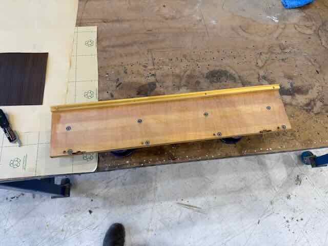 A wooden skateboard with a yellow edge resting on a work table in a workshop.