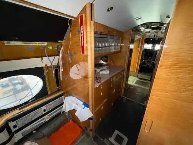 Inside a private jet, showing a wooden cabinet, a TV mounted on the wall, and an emergency exit door.