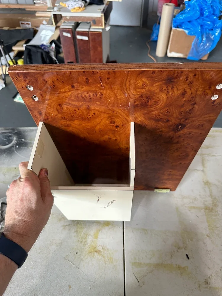 Viewing the inside of a wooden cabinet or shelf unit with a polished top surface and two internal compartments, held by a person's hand in a workshop setting.