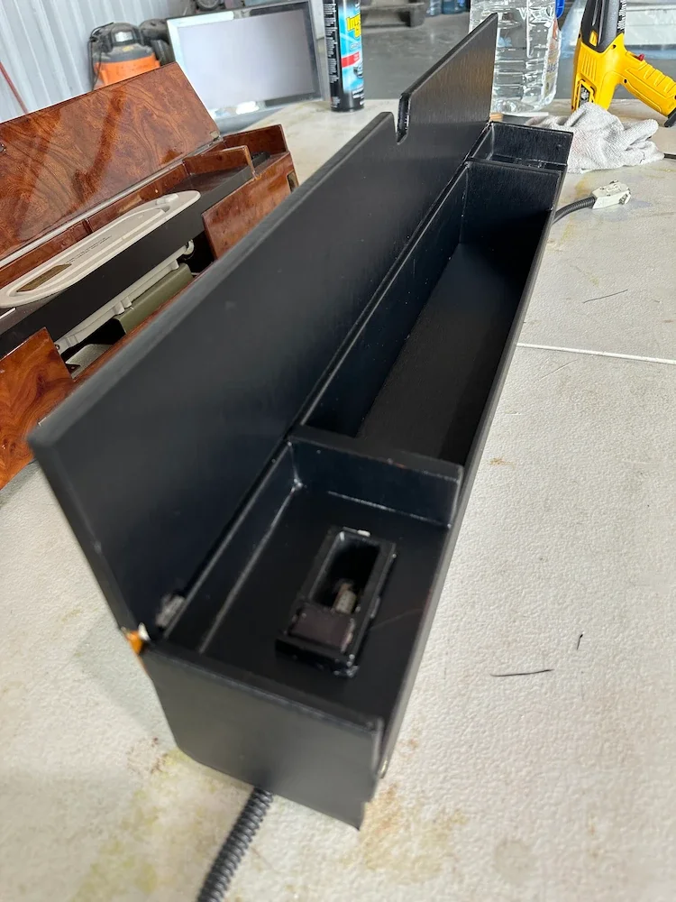 Black metal organizer with sections, placed on a workbench with tools, wires, water bottle, and other items in the background.