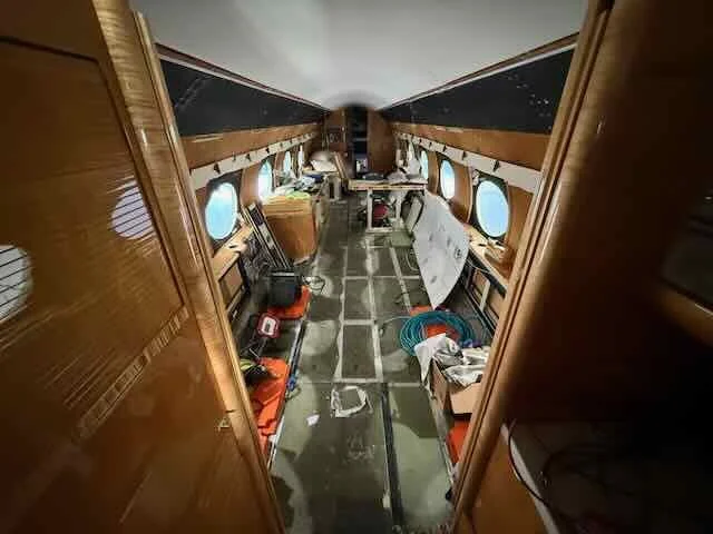 Interior of an airplane cabin under maintenance with tools and equipment scattered along the aisle.