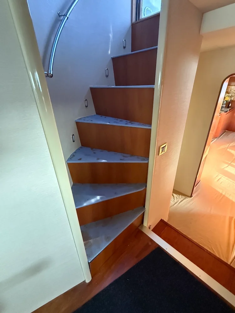 Photo of a small wooden staircase with marble steps leading up, next to a wall with a metal handrail, in a cozy indoor setting.