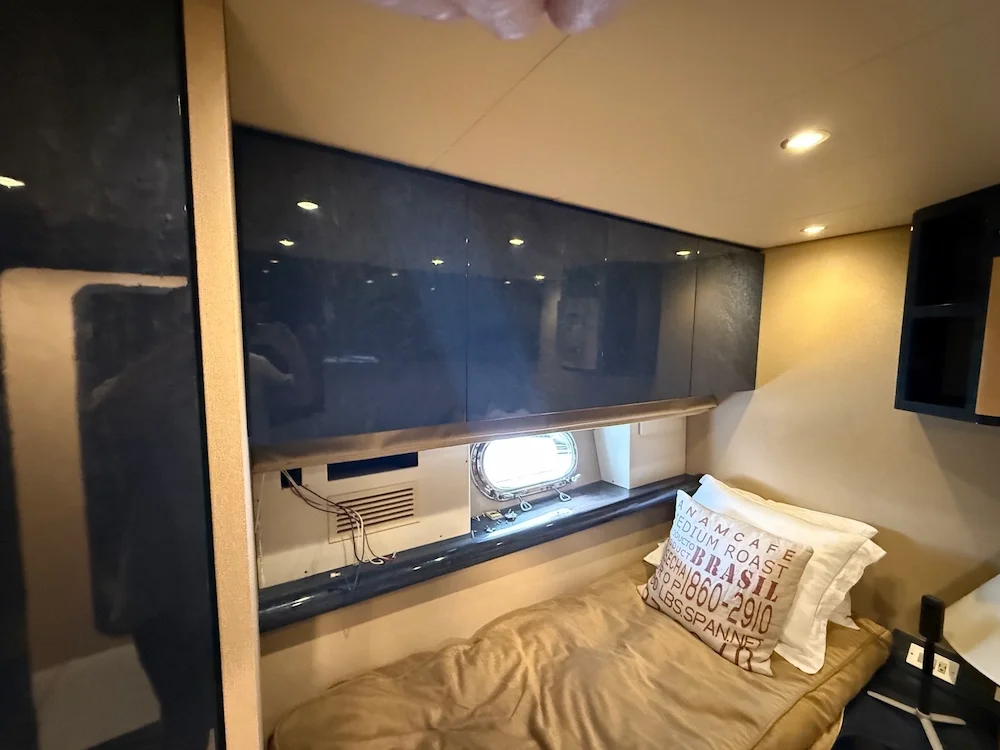 Small bedroom with a single bed, pillow, small window, overhead lighting, and dark, glossy cabinets.