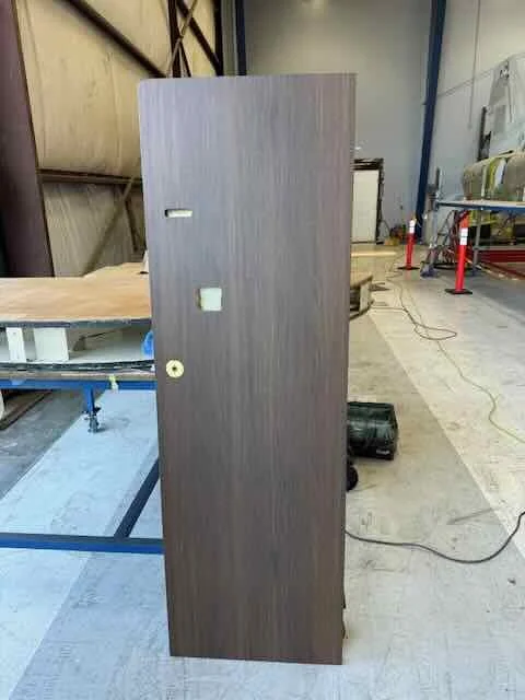 A dark wooden door leaning upright in an industrial workshop with tools and equipment in the background.