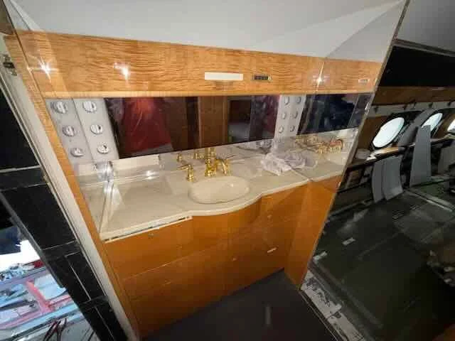 A bathroom vanity with a curved cream-colored sink, gold fixtures, and a mirror, with a wood-paneled cabinet above and a white marble countertop.