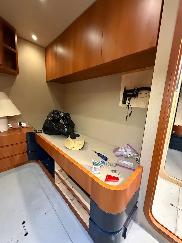Interior of a room under renovation with a partially assembled wooden desk, various tools, screws, and a black bag on top.