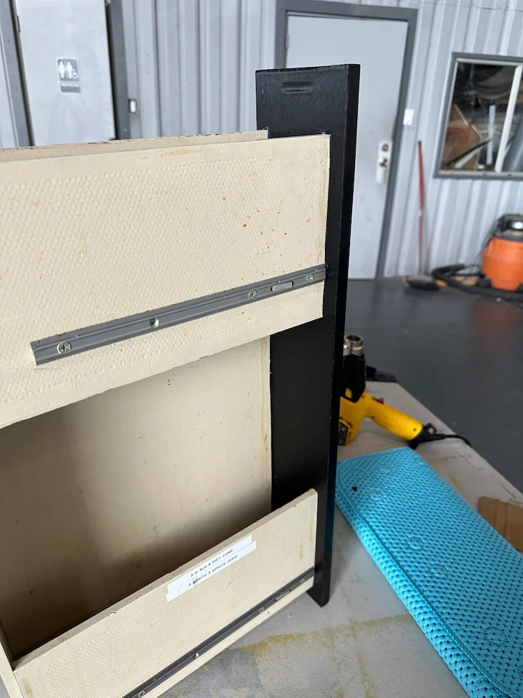 Close-up of a partially assembled wooden or composite cabinet or panel with metal brackets in a workshop.
